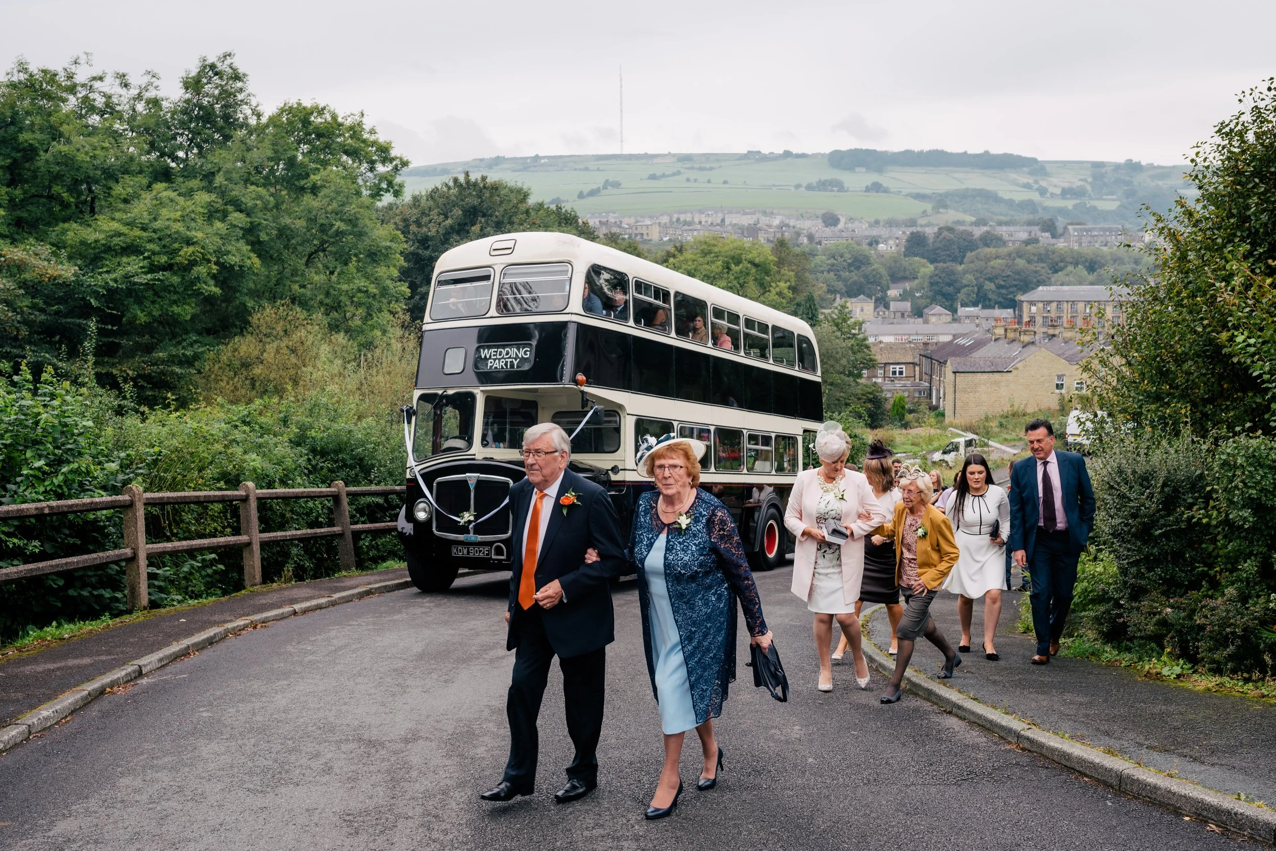 Group of people, including elderly, walking away from a vintage double-decker bus with a 