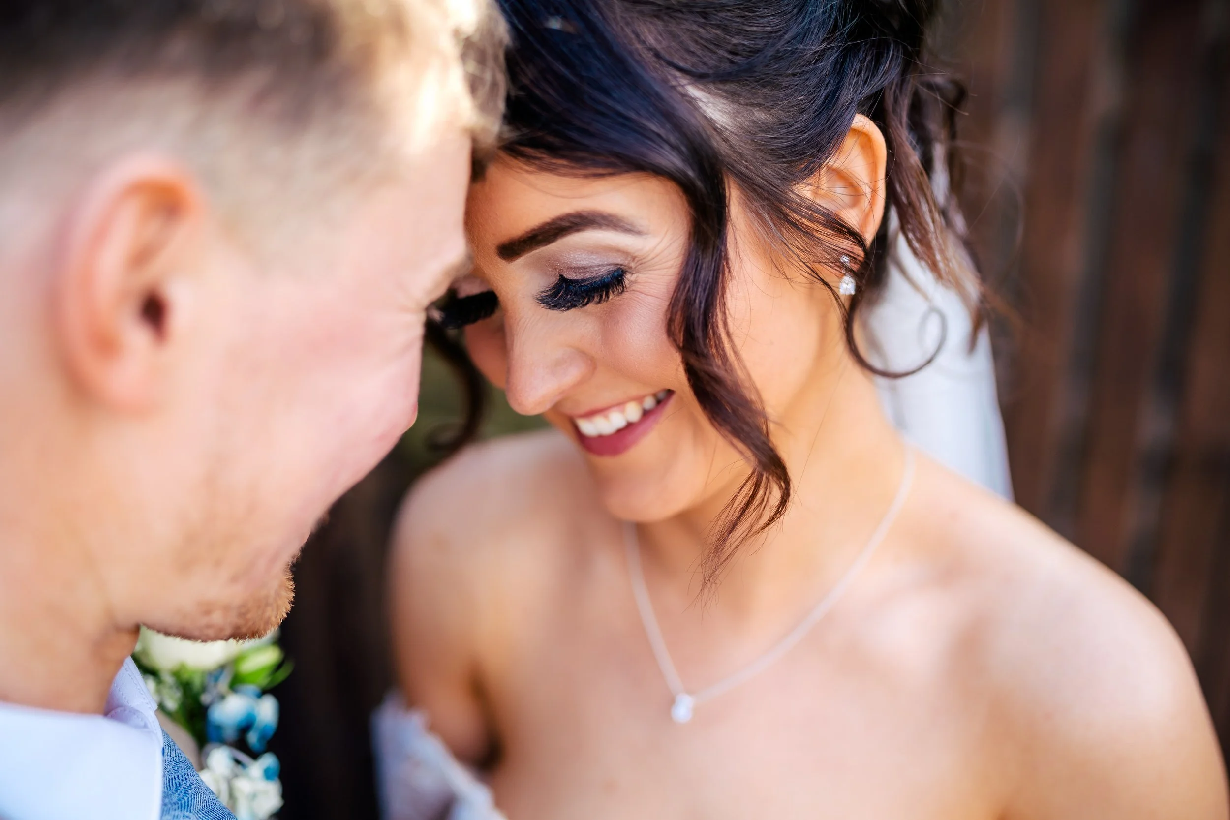 Close-up of a couple smiling, with their foreheads touching, at a wedding or special event.
