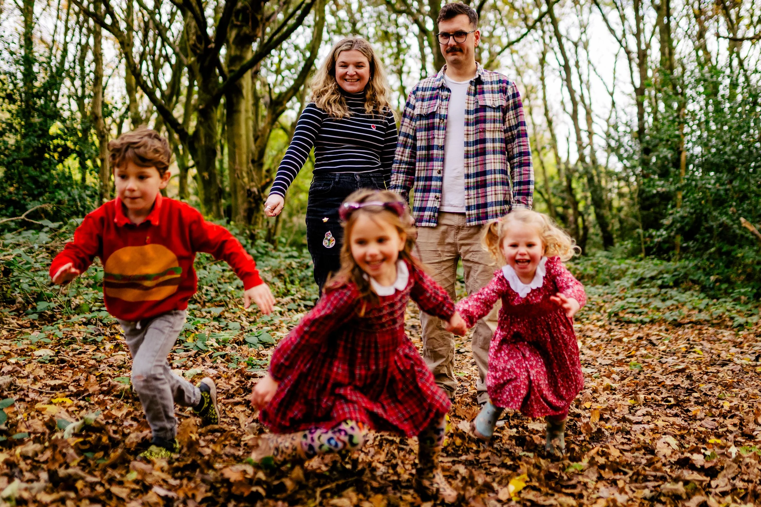 A family of six enjoying a hike through a wooded area during fall, with children playing and adults smiling.