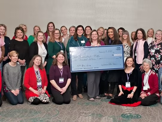 Group of women and a girl holding a large check for $2,300 at an indoor event.