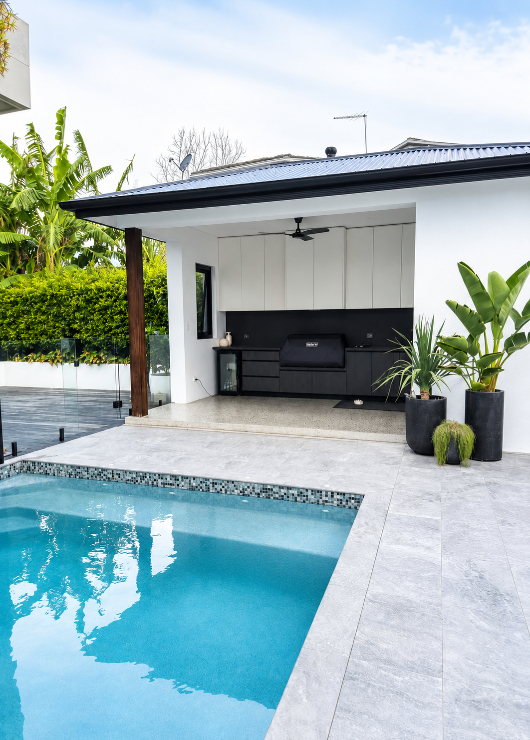 Outdoor pool area with a covered outdoor kitchen and greenery.