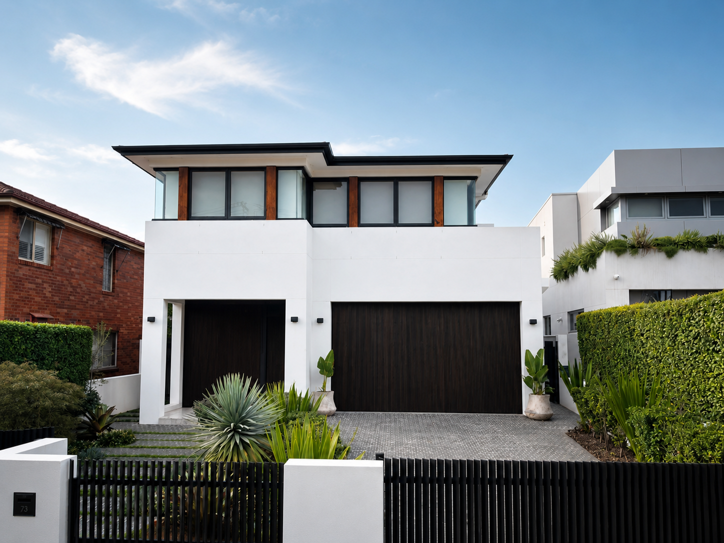 Modern white two-story house with large windows, black garage door, and surrounding greenery including potted plants and neatly trimmed bushes.