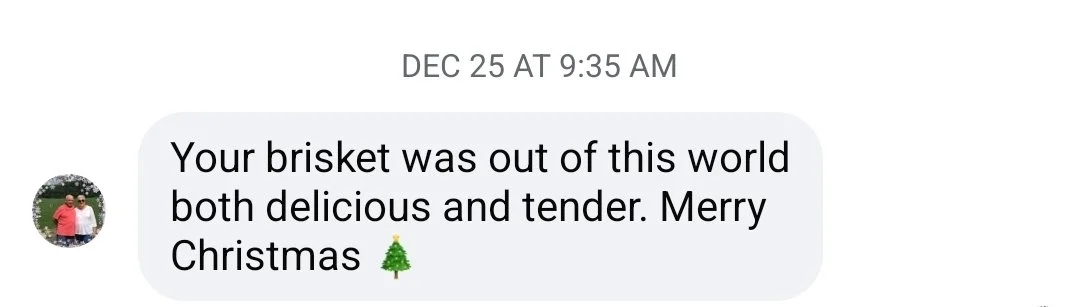 Text message on a phone screen reading: "Your brisket was out of this world both delicious and tender. Merry Christmas" with a Christmas tree emoji.