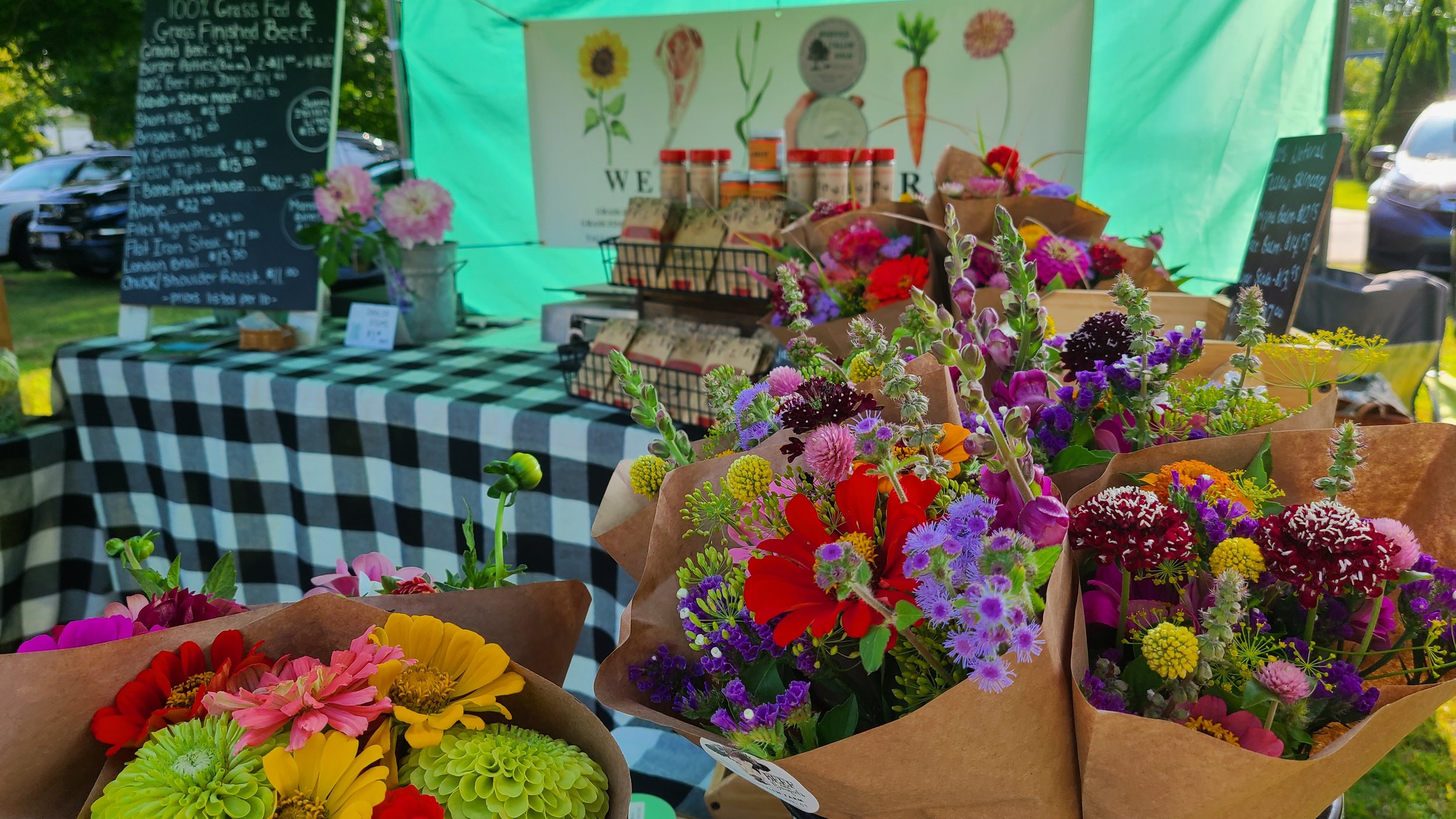 Various colorful flower bouquets on display at a farm stand with a black and white checkered tablecloth and a menu board in the background.