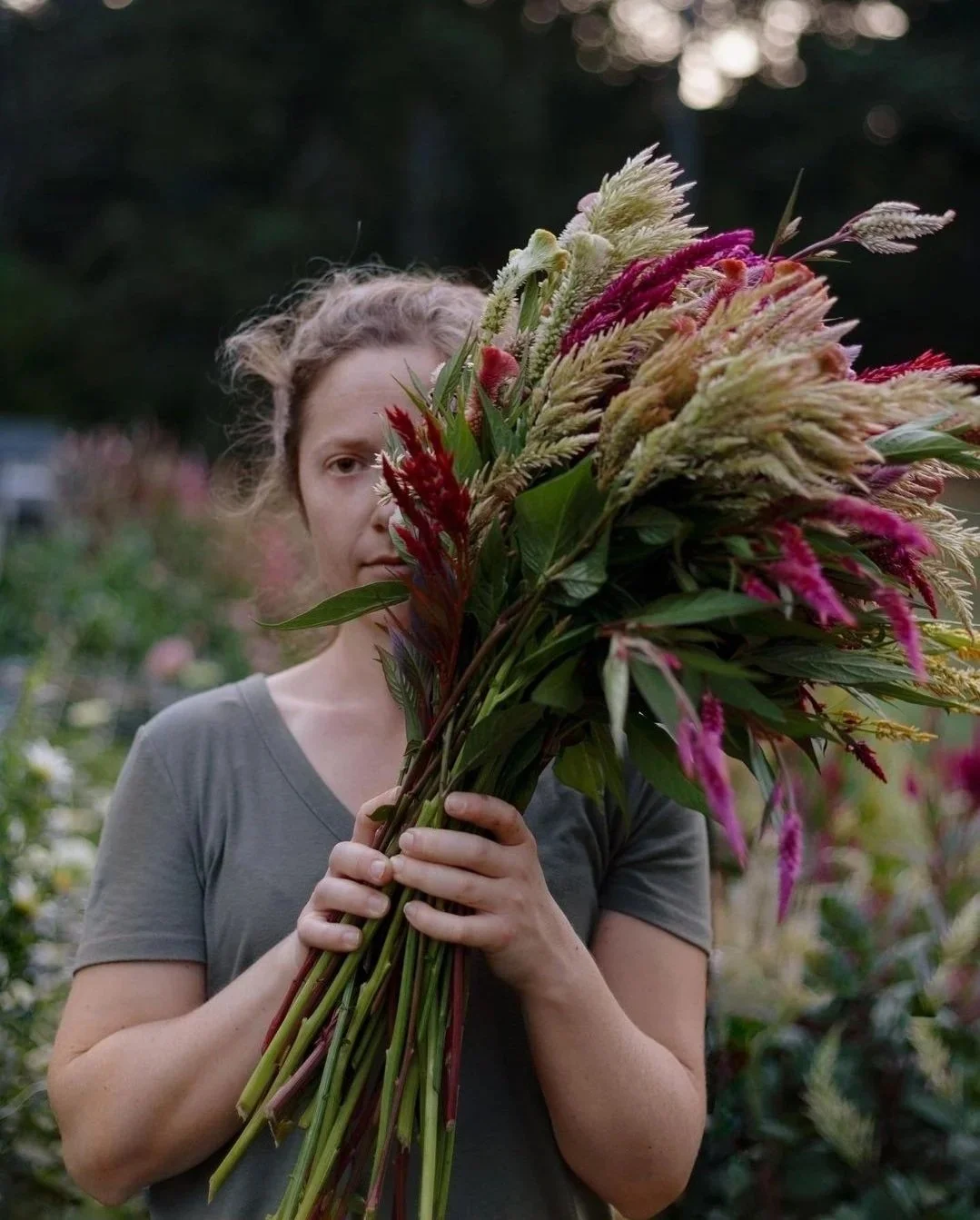A woman holding a large bouquet of colorful flowers outside in a garden.