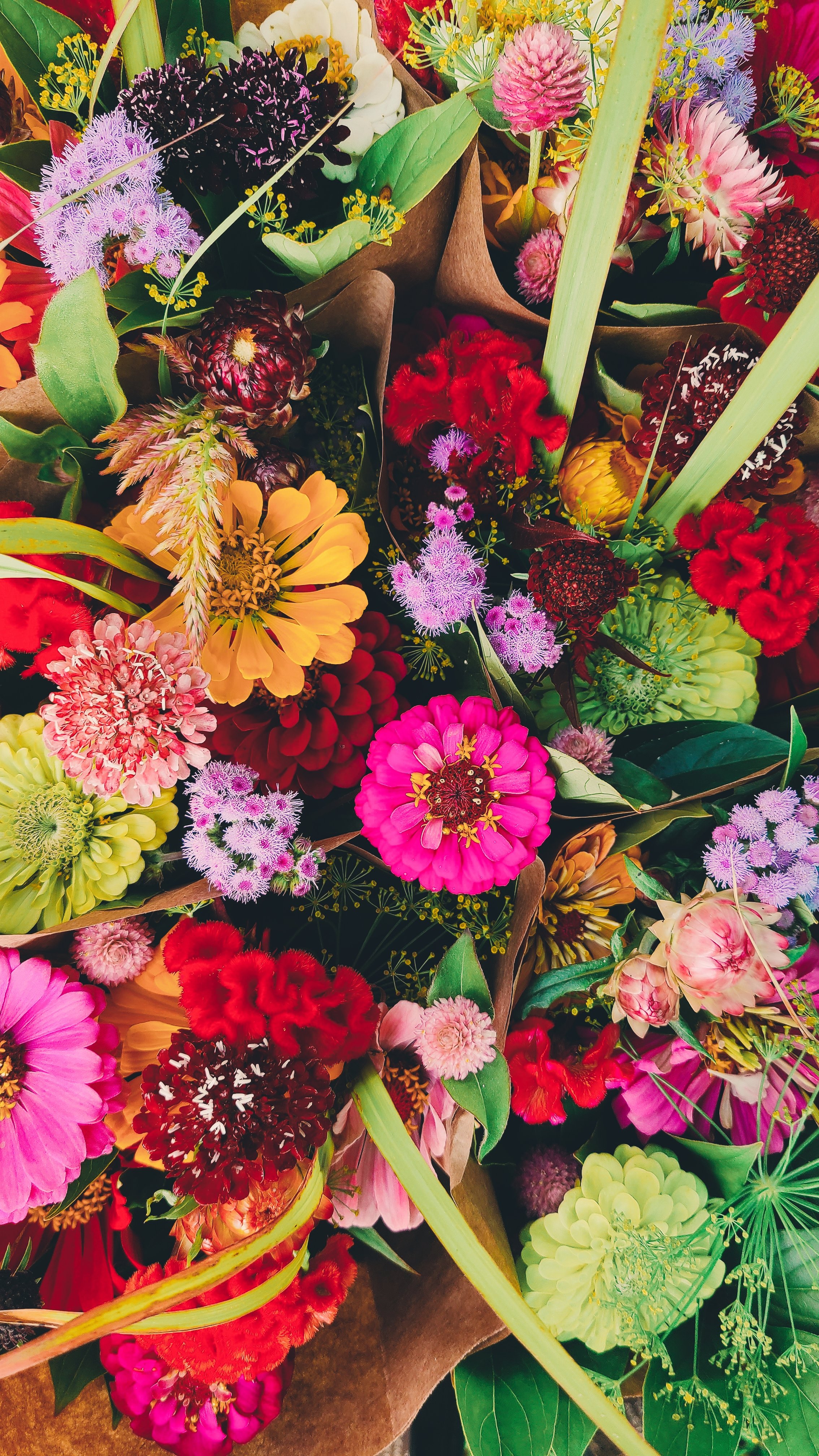 A vibrant mix of colorful flowers including pink, red, purple, orange, yellow, and green, arranged in a bouquet.