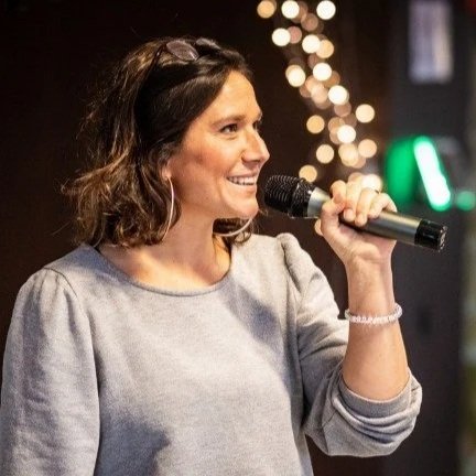 Une femme souriante tenant un microphone lors d'une performance ou d'une présentation en intérieur.