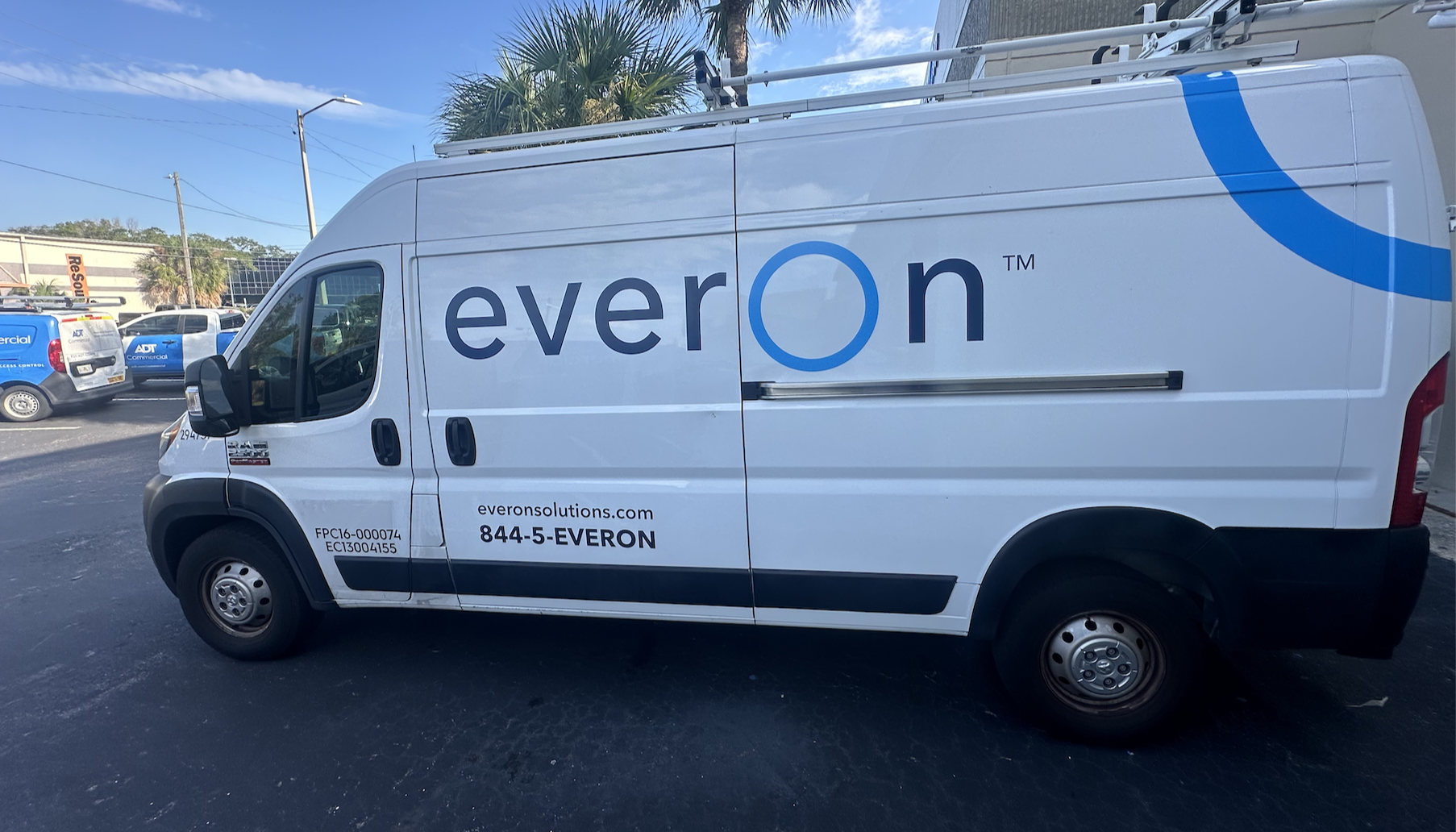 A white commercial van with the word 'everOn' displayed on the side, parked in a lot with other vehicles and palm trees in the background.