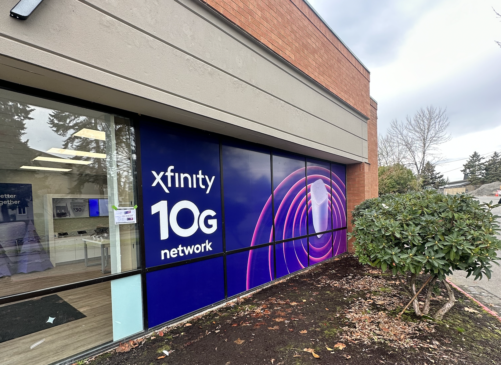Exterior of a store with a large sign advertising Xfinity 10G network, featuring a microphone graphic with concentric purple rings.