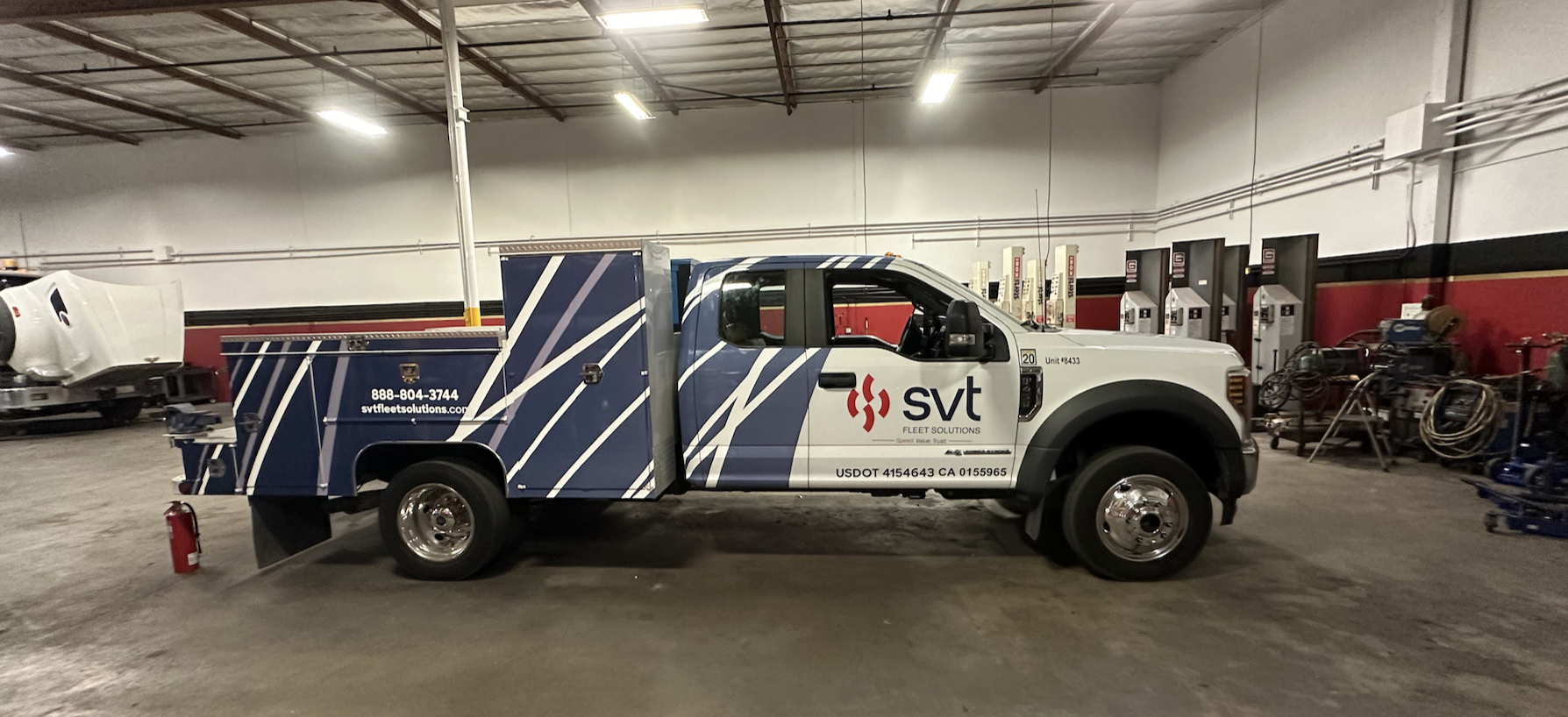 A fleet services truck with the logo 'SVT Fleet Solutions' parked inside a garage or warehouse, with equipment and shelving along the walls.