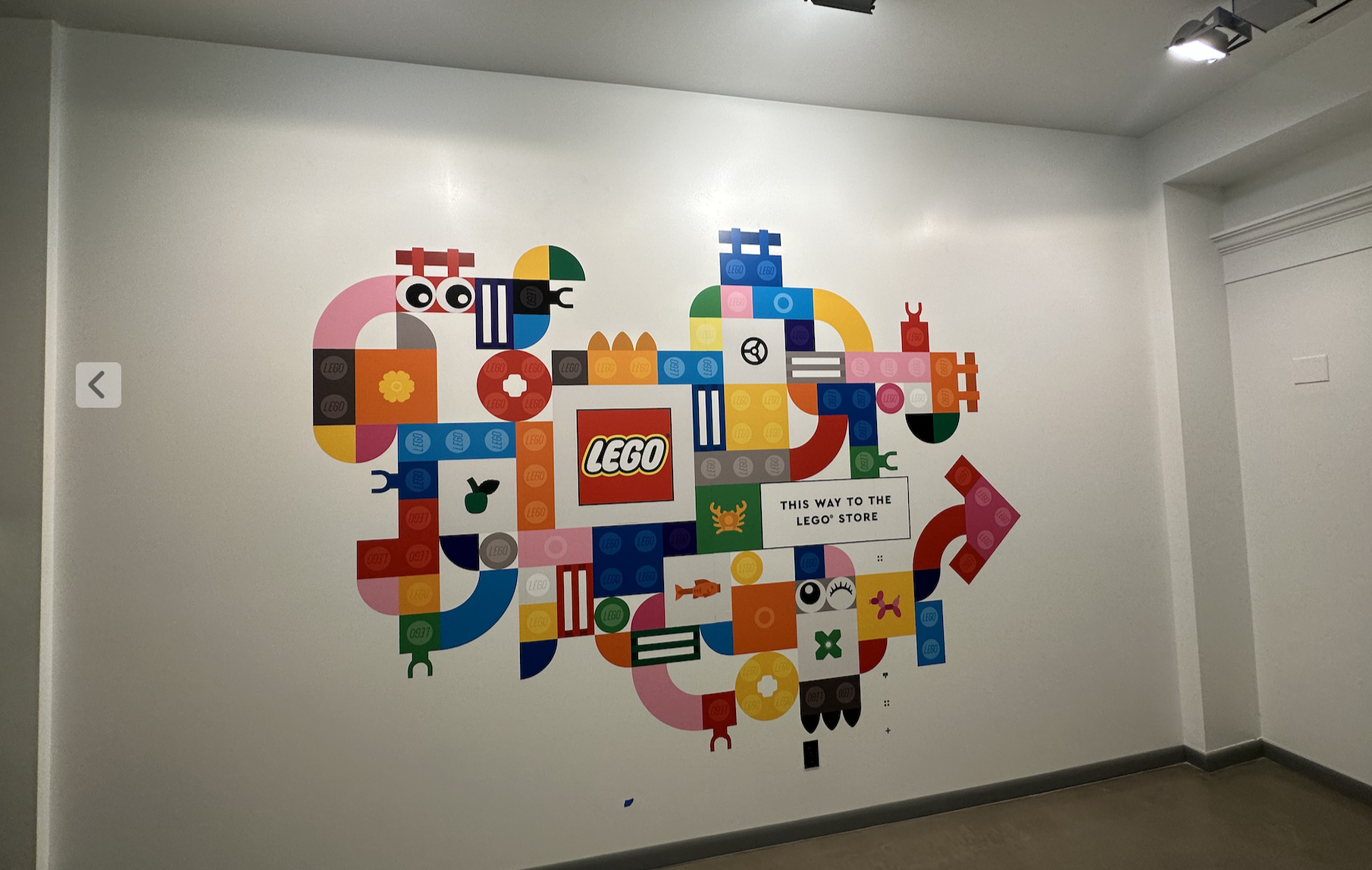 Colorful LEGO-themed wall decoration with an arrow pointing right, and a sign that says 'This way to the LEGO store'.