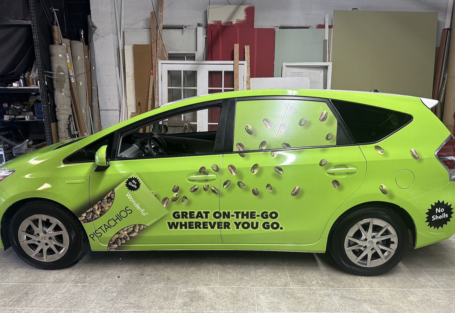 A bright green car with advertisements for pistachios, including the phrases "GREAT ON-THE-GO WHEREVER YOU GO" and "No Shells," parked inside a workshop or garage.
