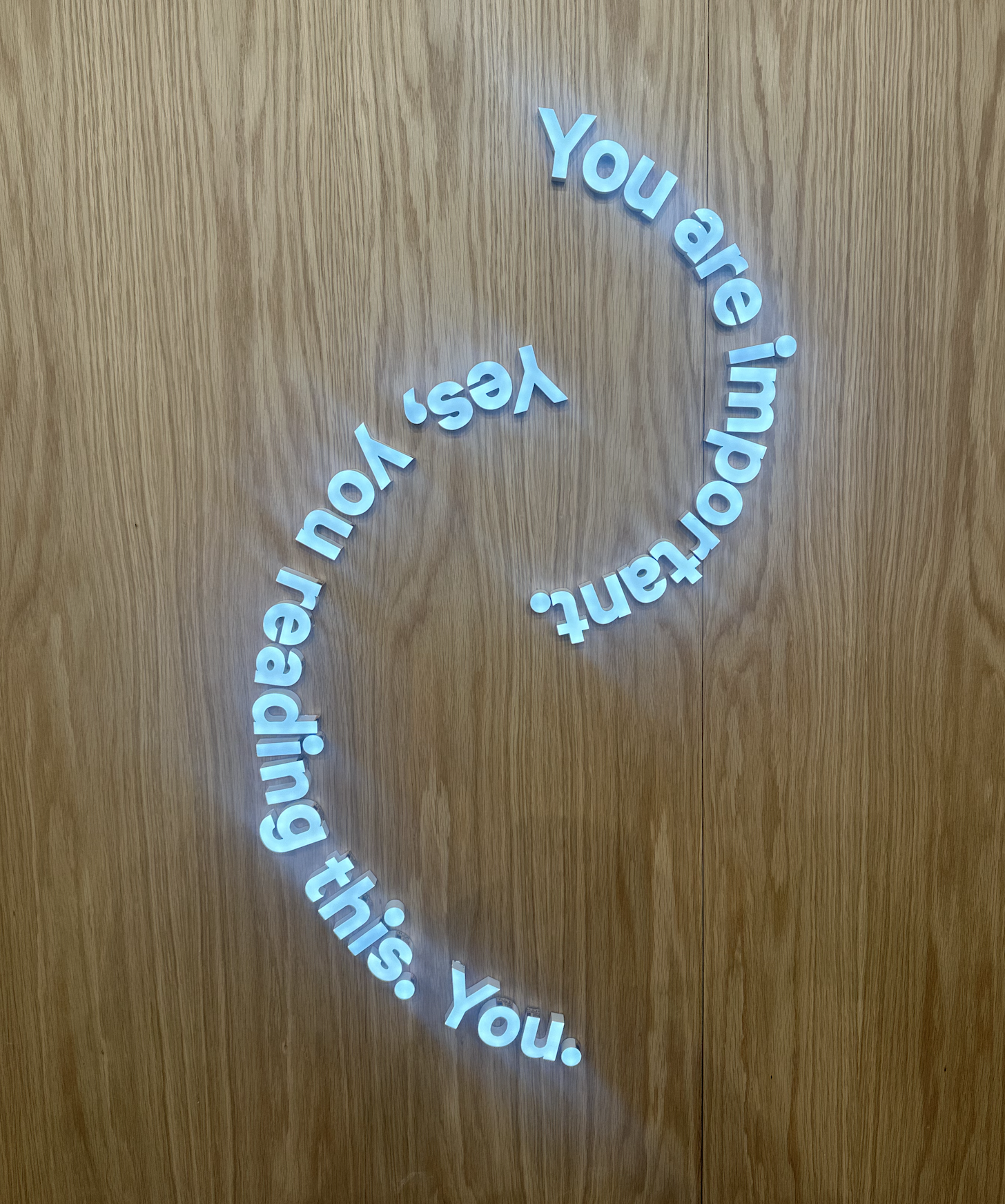 Circular arrangement of white 3D letters on a wooden wall spelling out "You are involving this. Yes, you."
