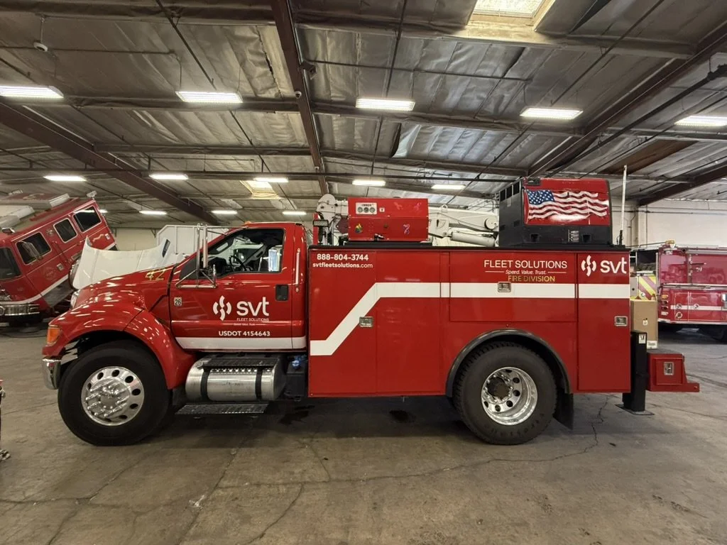 Red fire truck inside a garage with other emergency vehicles in the background.