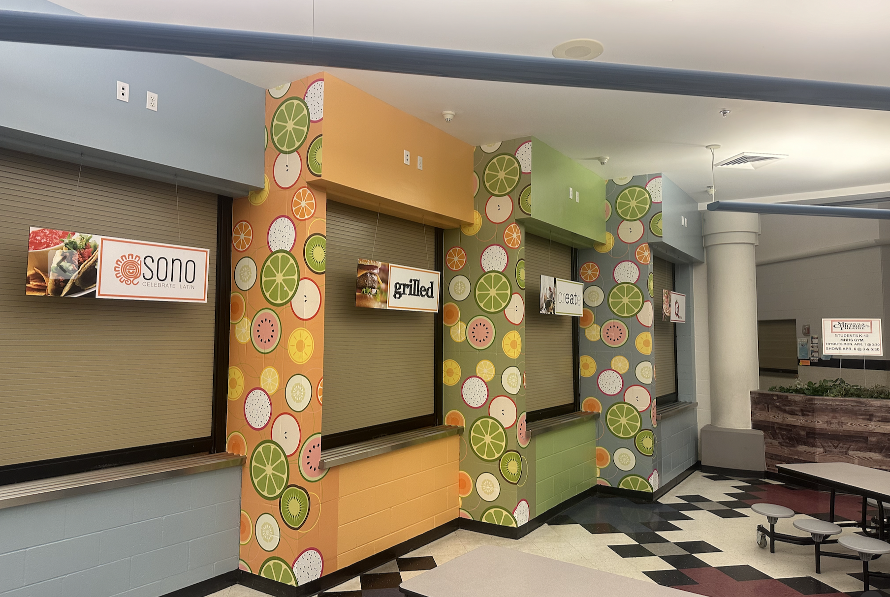 Closed food stand with colorful fruit-patterned decor, with signs indicating options like 'sono' and 'grilled', and a seating area nearby.