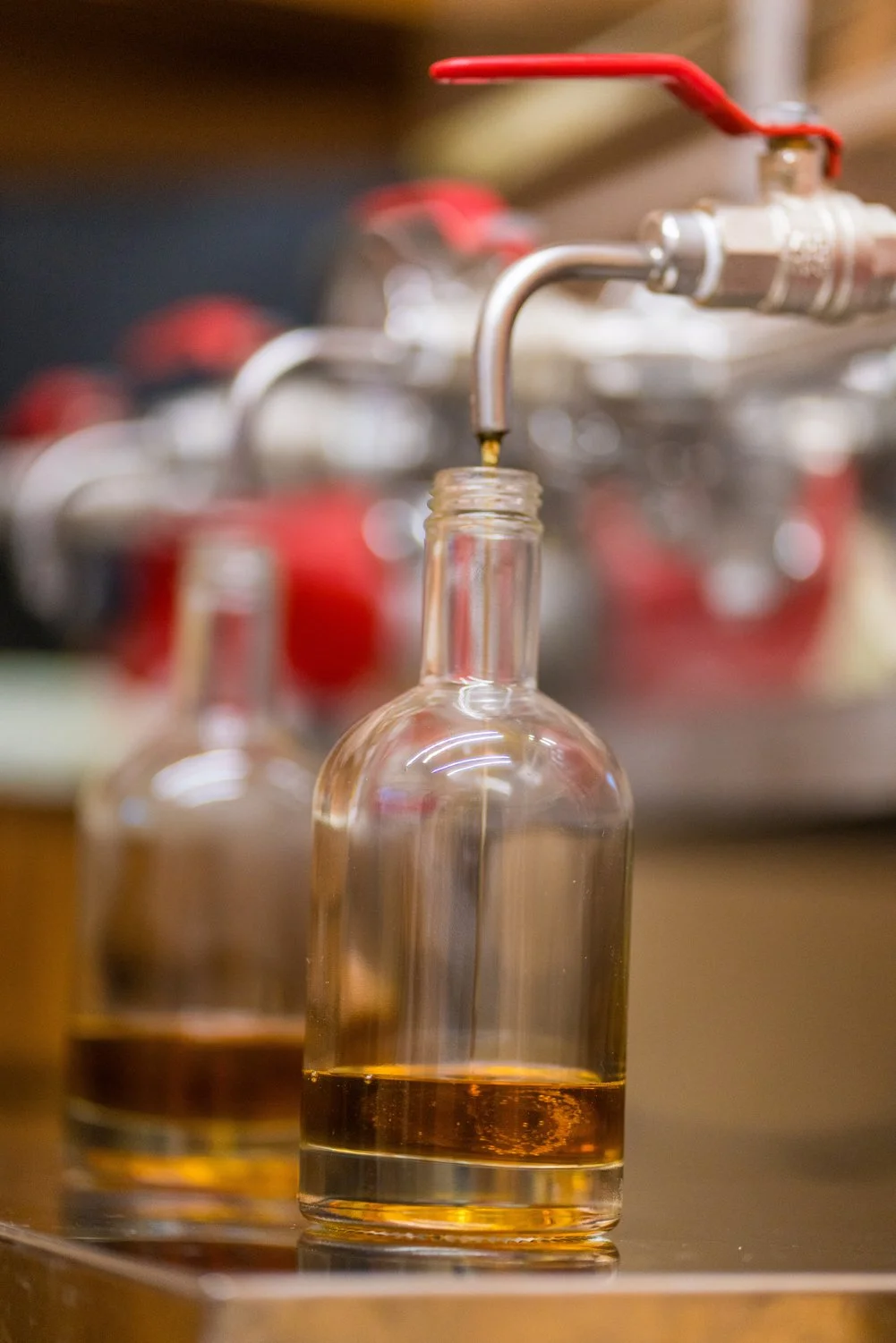Bottle being filled with maple syrup through a spout during the processing process. Wholesale maple syrup in Ontario, bulk maple syrup Canada, custom maple syrup gifts, corporate maple syrup favours. Grade A maple syrup available for purchase.