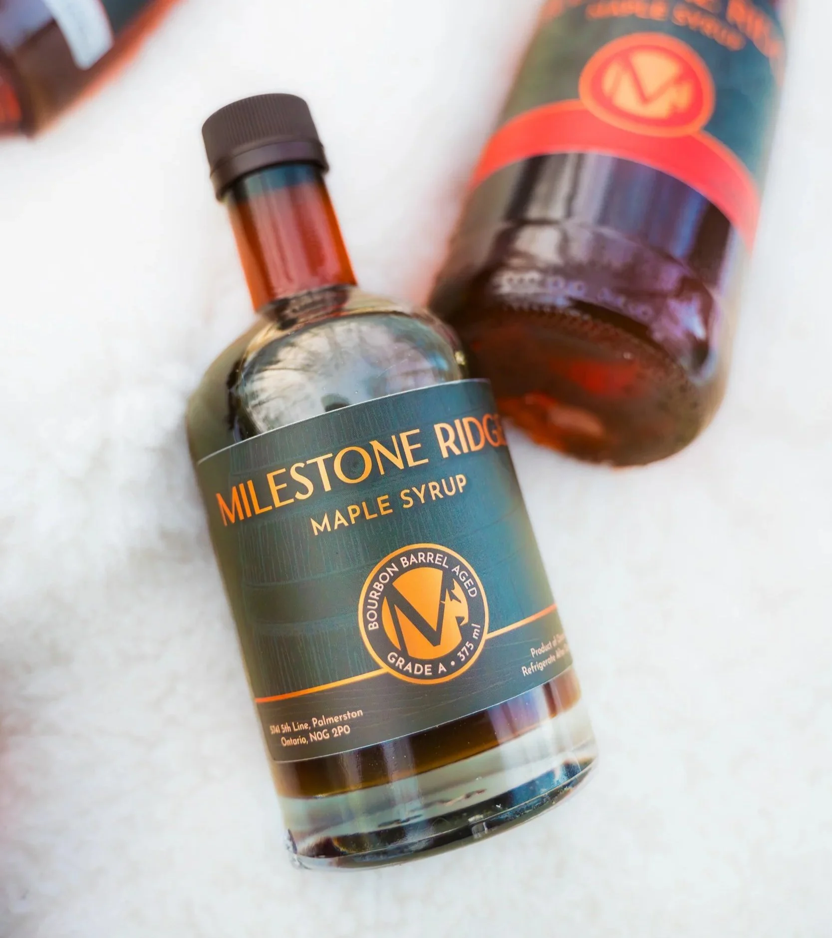 Close-up of a bottle of maple syrup with a black cap and a label that reads 'Milestone Ridge Maple Syrup' and additional product information at the bottom. Maple syrup in Palmerston Ontario, buy maple syrup near me, maple syrup Wellington County.