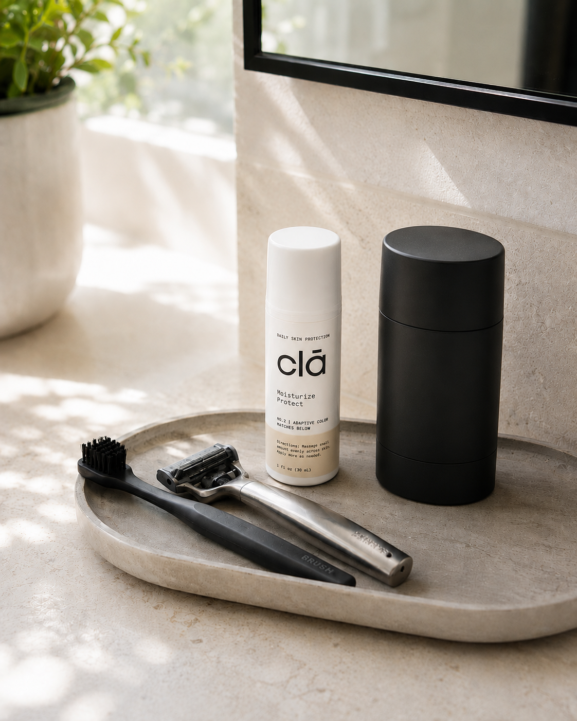 A bathroom countertop with a black storage container, a white body spray can labeled 'clā moisturize protect,' a black hairbrush, and a silver razor on a tray near a window with sunlight.