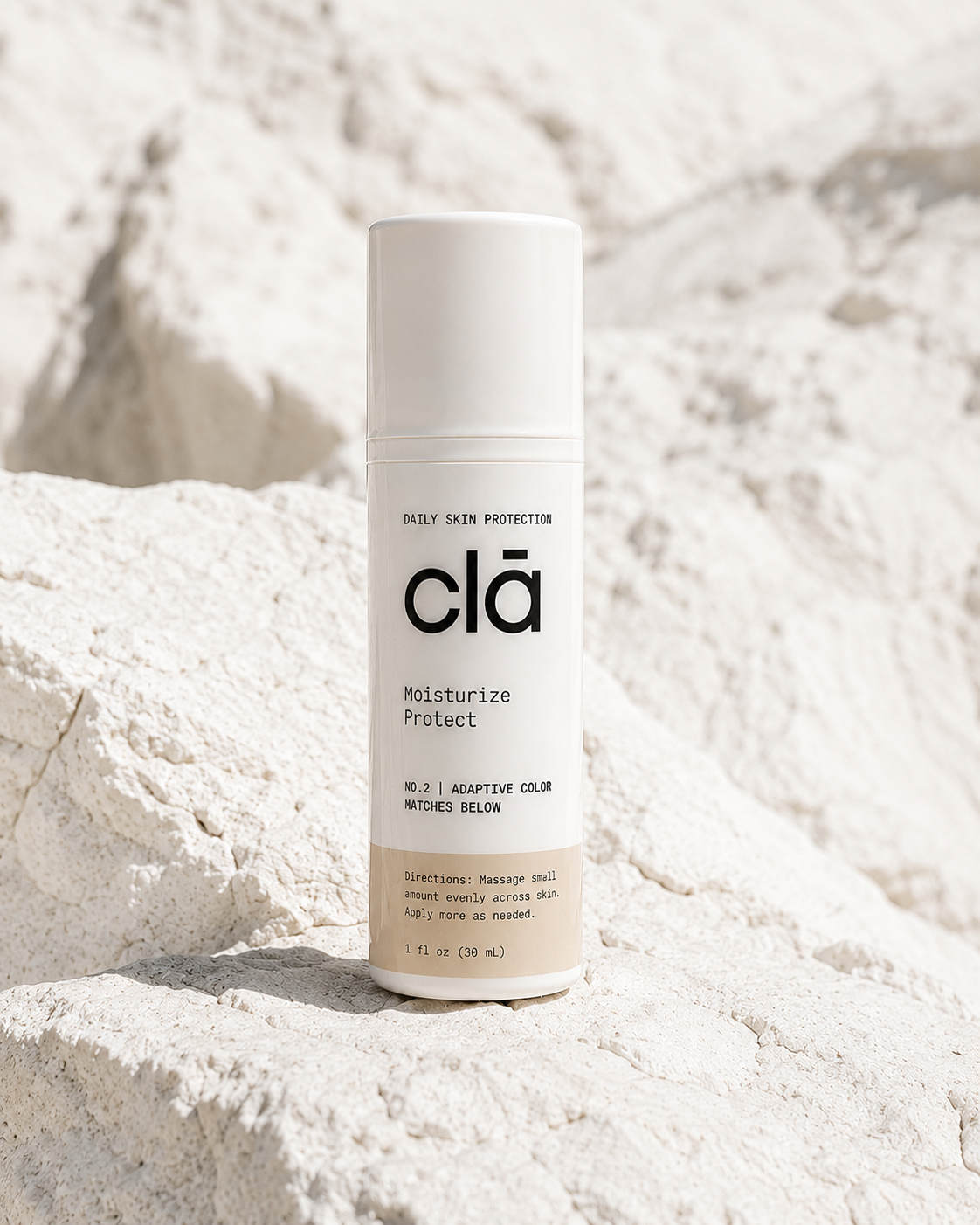 A white bottle of skincare product labeled 'clā' standing on sandy white rocks with a blurred white rocky background.