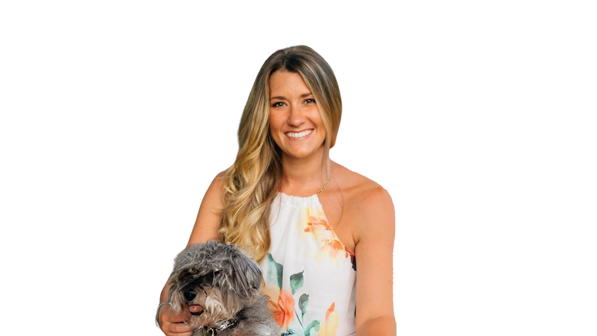 A young woman with long blonde hair and a bright smile, wearing a sleeveless floral dress, is holding a small dog with fluffy gray and black fur.