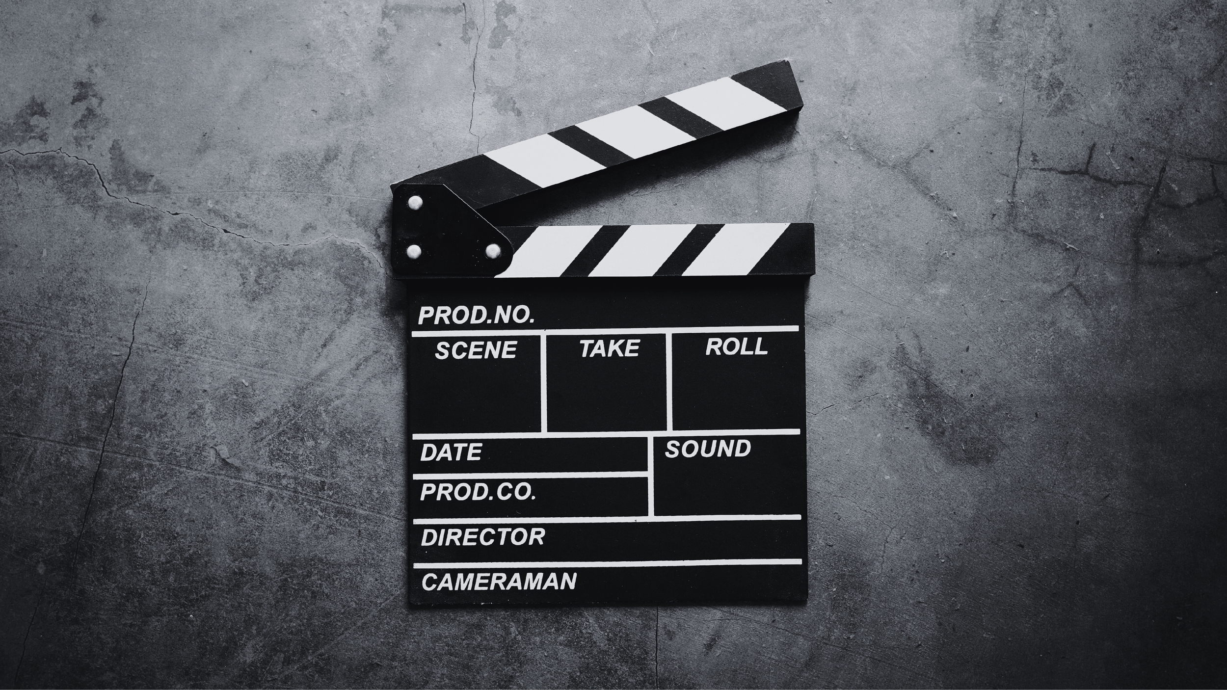 A traditional black and white film clapperboard resting on a cracked gray concrete surface.
