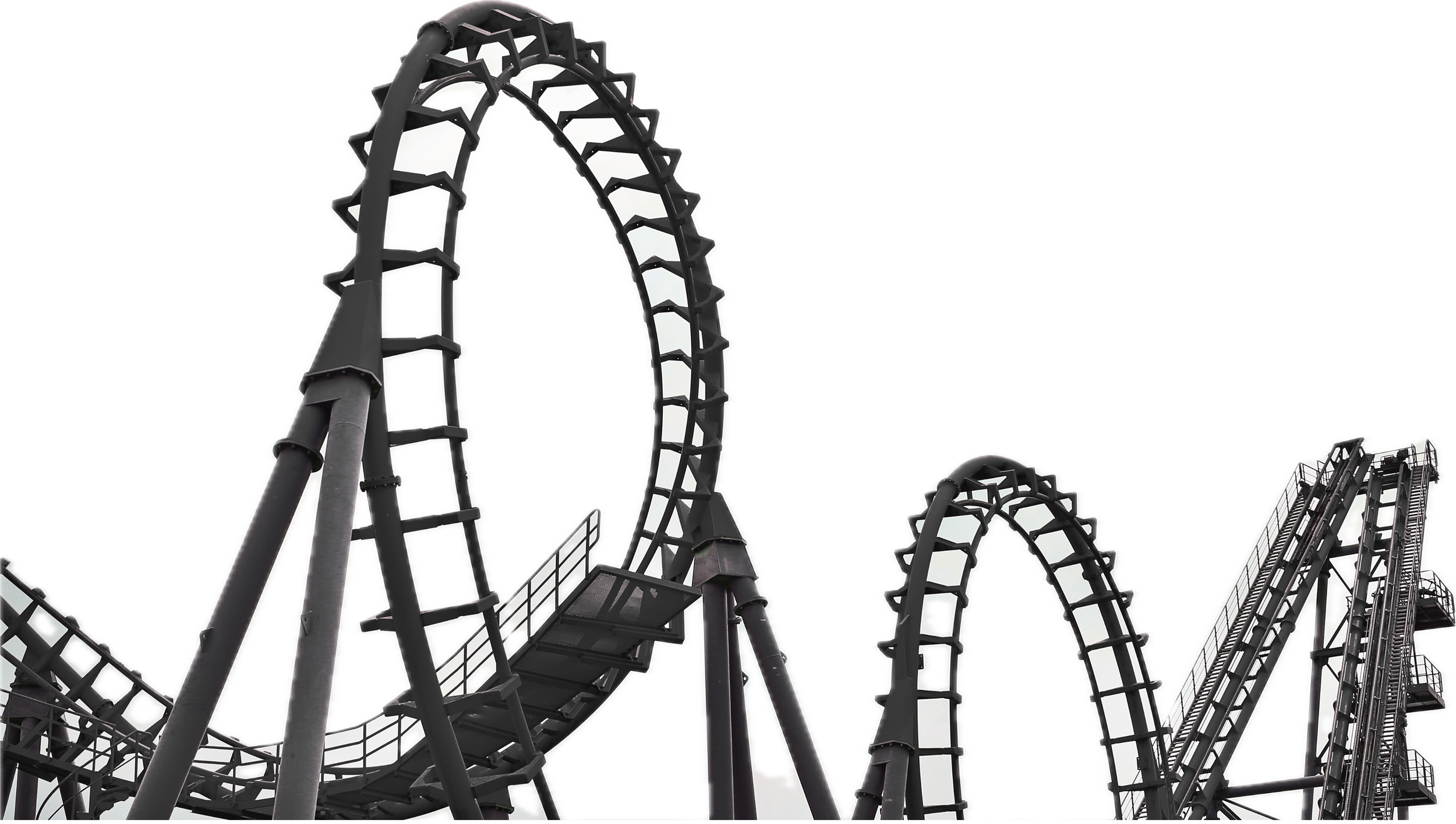 A black roller coaster with steep drops and sharp curves viewed from below against a white sky.