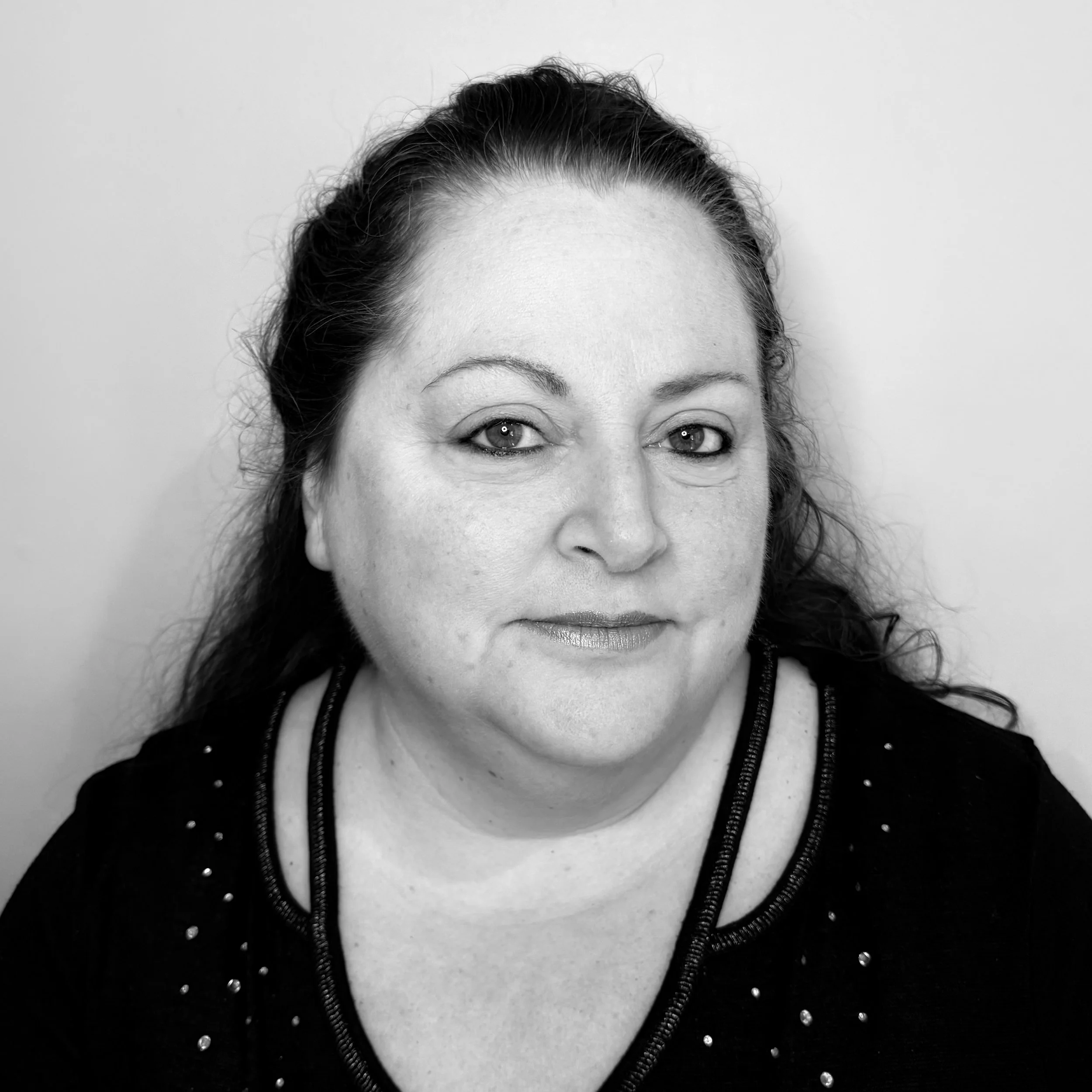 Black and white portrait of a woman with wavy hair, looking at the camera with a slight smile, wearing a dark top with embellishments.