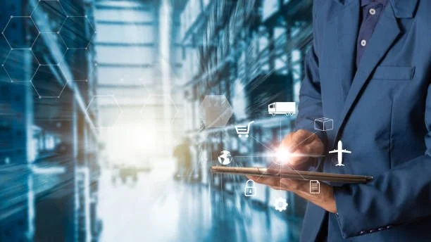 A person in a suit holding a tablet with various digital icons floating around in a modern, glass-covered building