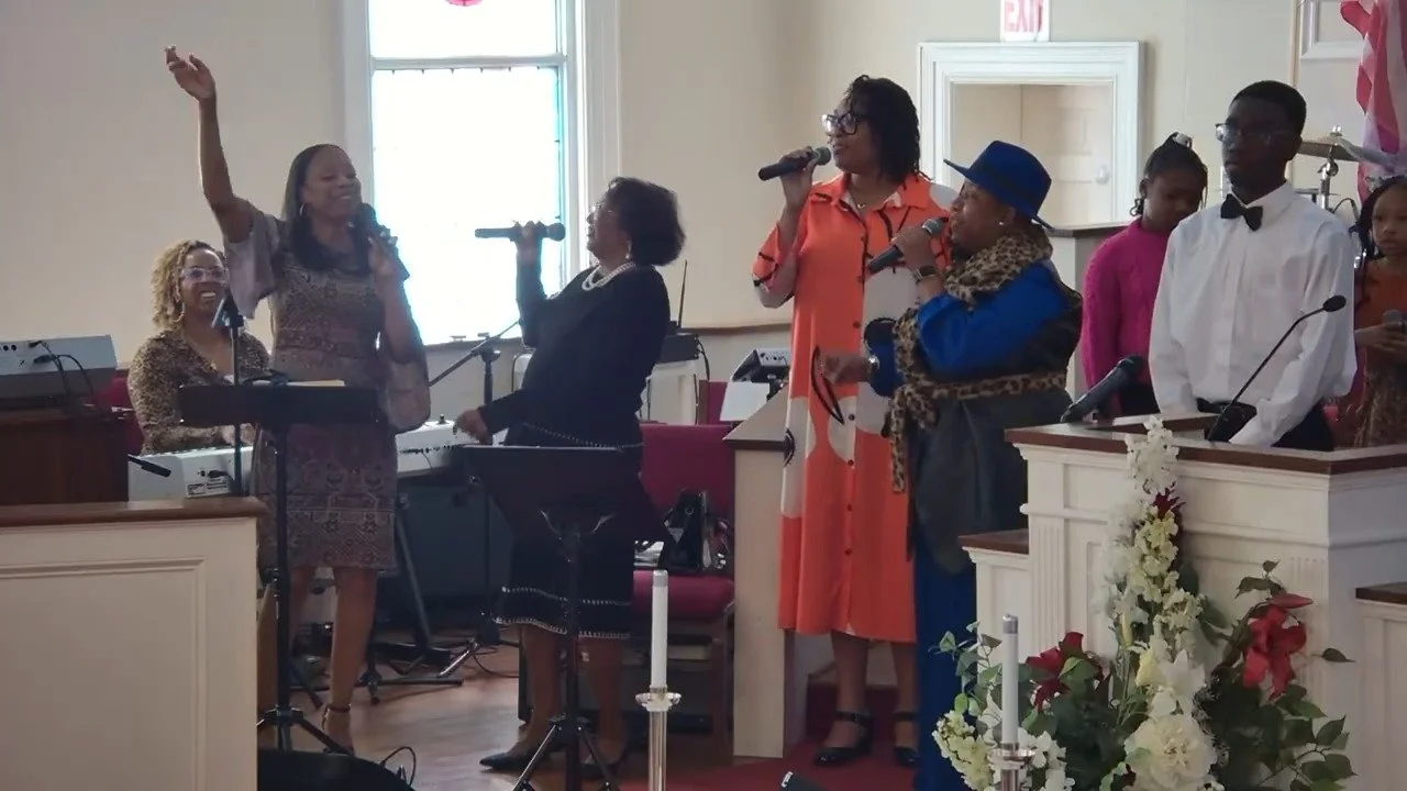 A group of people singing and playing music in a church, with some holding microphones and others playing instruments.