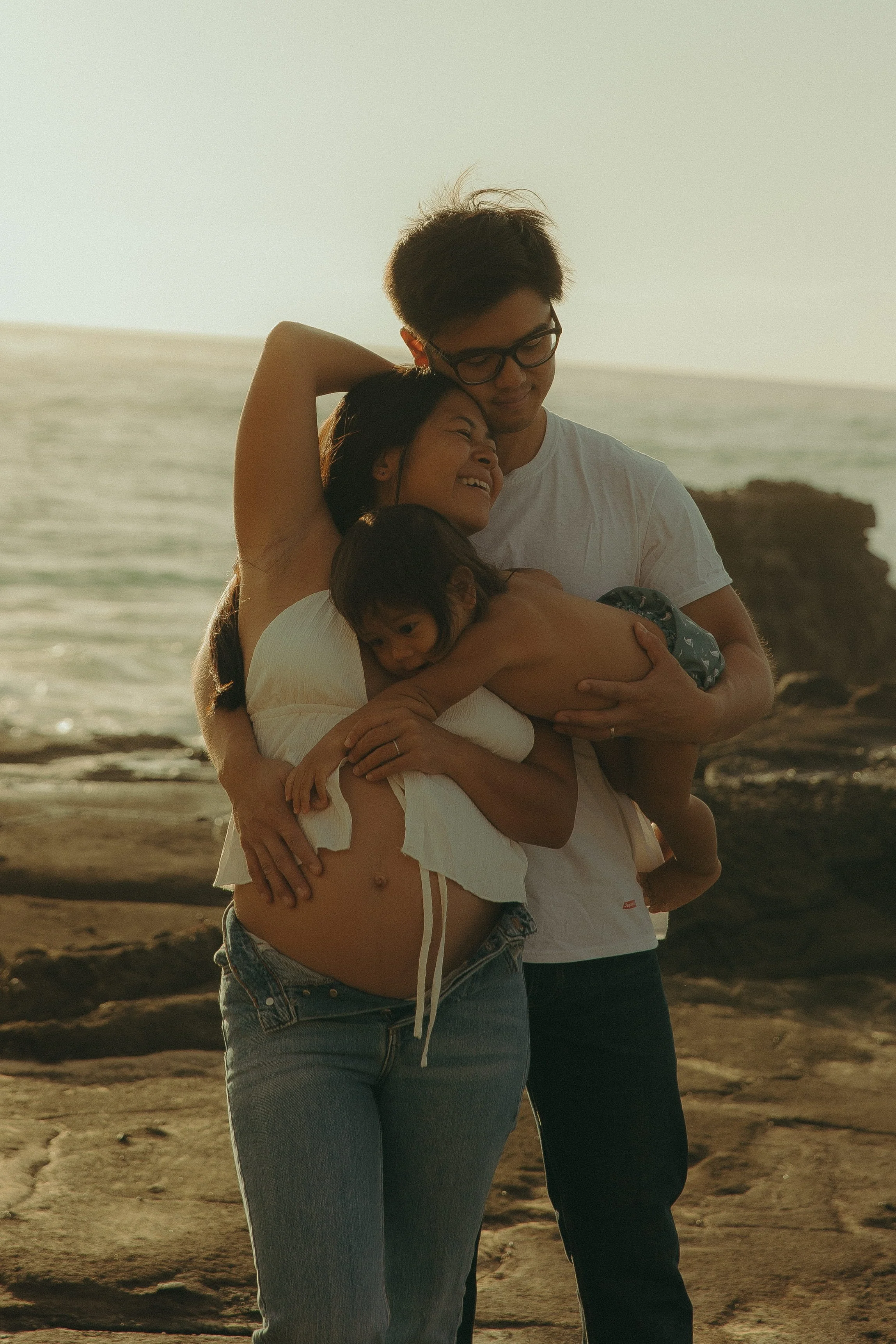 Oahu beach family of three hugging at sunset