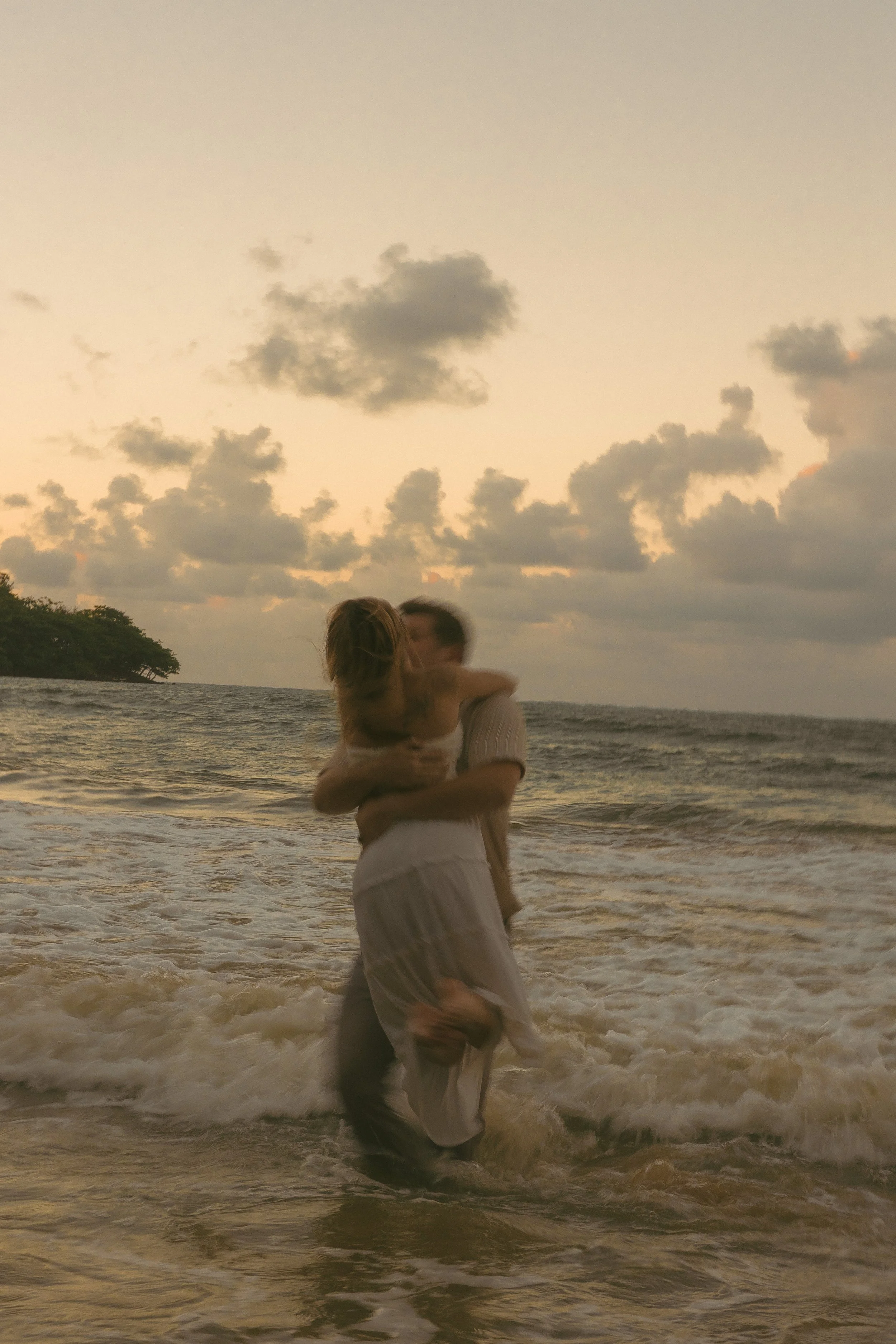 Couple kissing in the waves at sunset on Oahu's North Shore, motion blur and warm golden sky, cinematic couples photography by Maggie T Photography