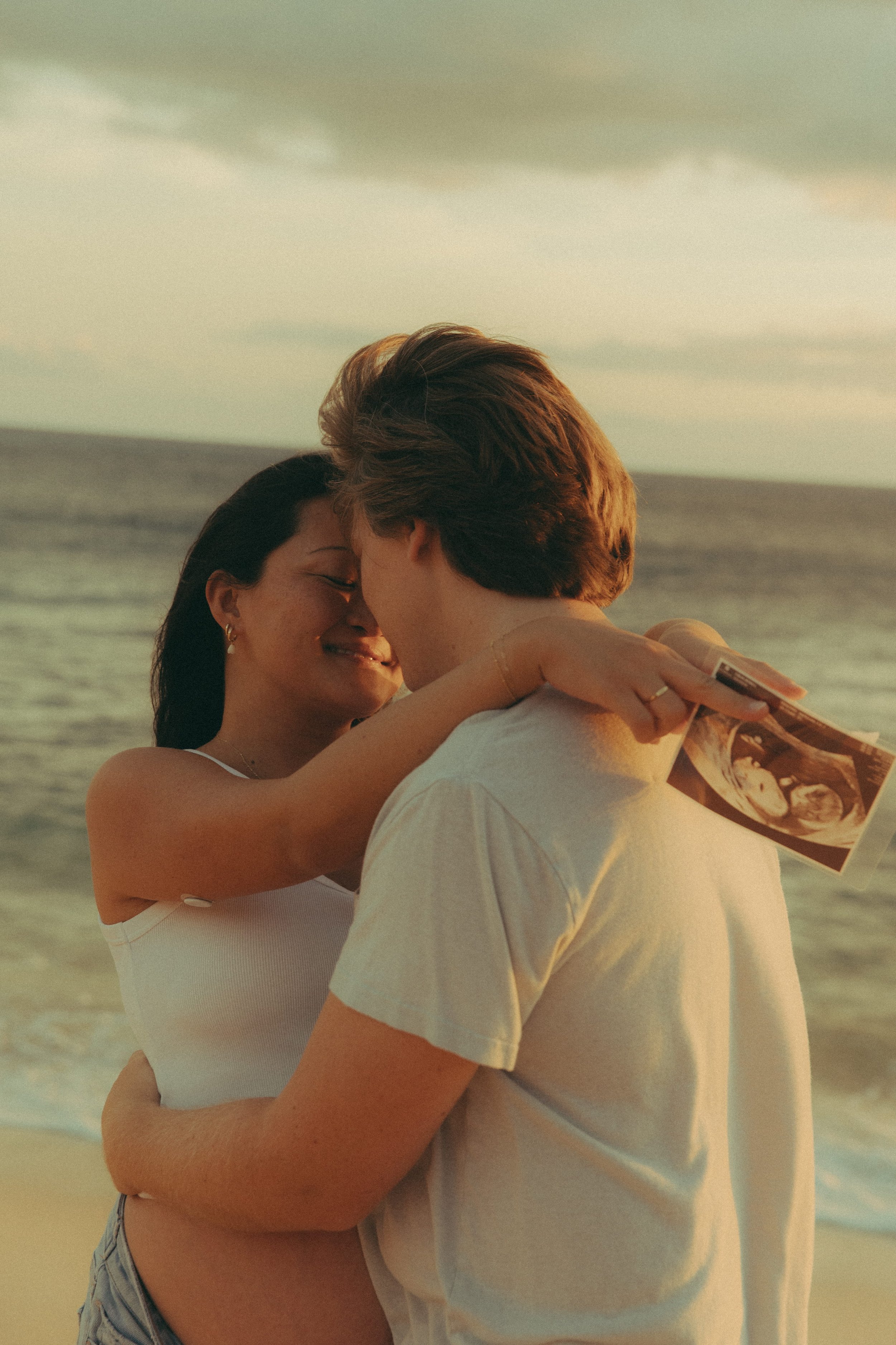 Oahu beach maternity photography session holding ultrasound photo