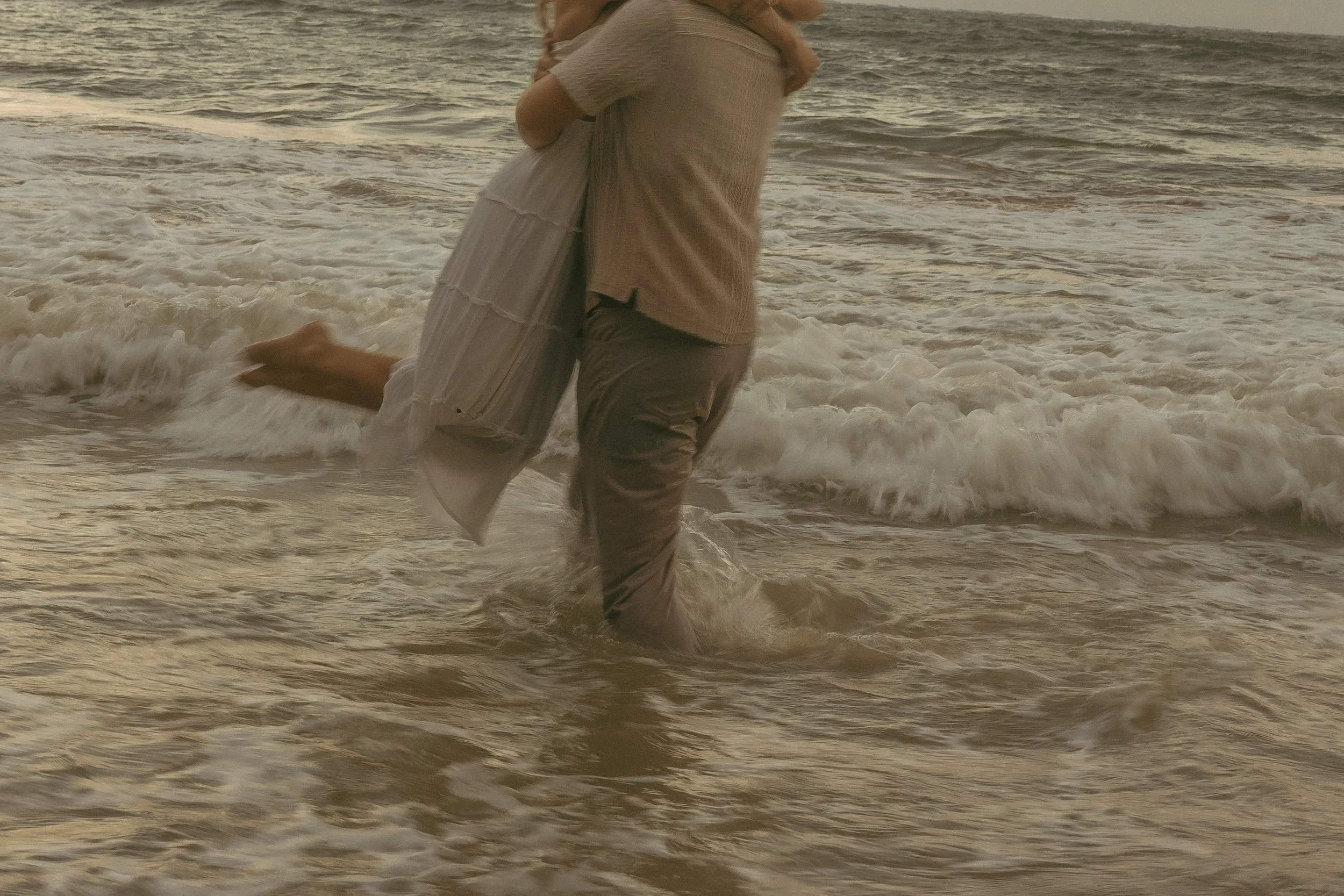 Man lifting woman in the crashing waves on North Shore Oahu, film-toned motion blur couples session, cinematic beach photography by Maggie T Photography