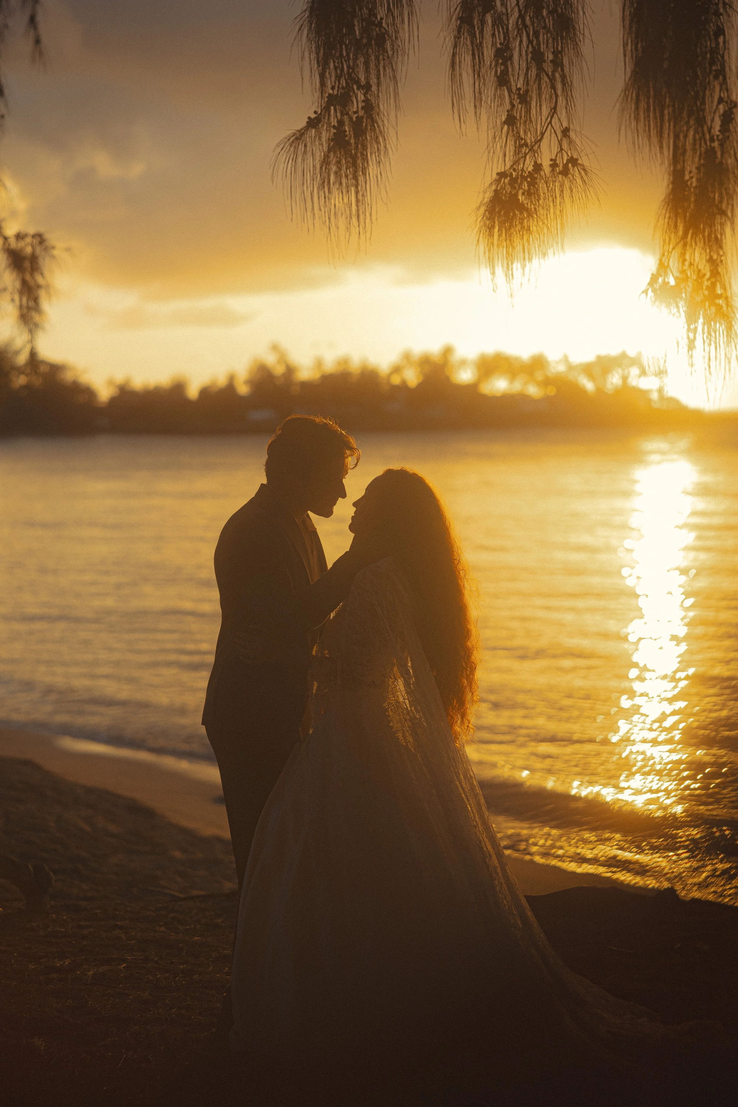Silhouette of bride and groom embracing on an Oahu beach at golden sunset, film-toned elopement portrait