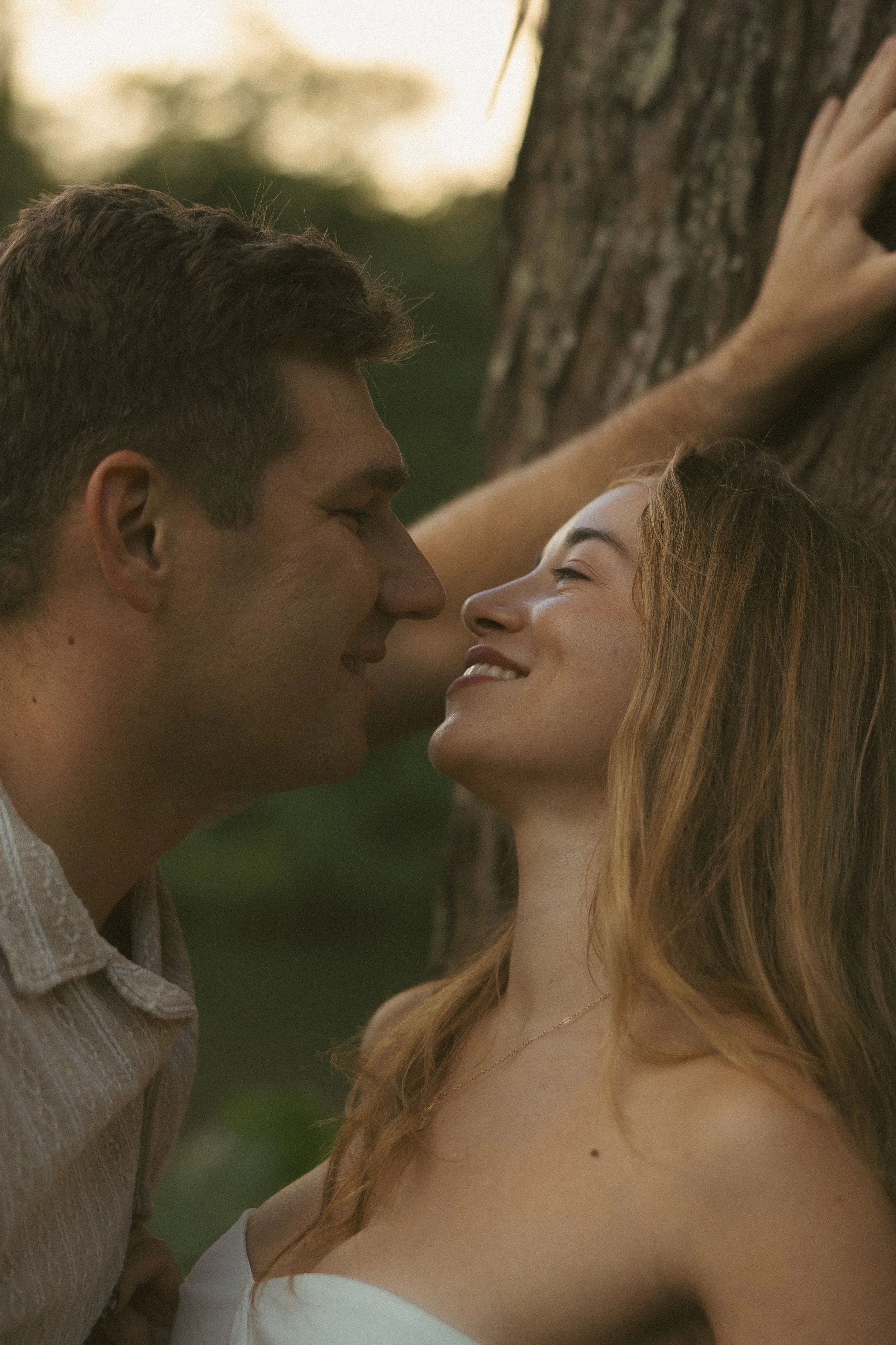 Close up of couple nearly kissing against a tree trunk in warm golden hour light, intimate couples session by Oahu photographer Maggie T Photography