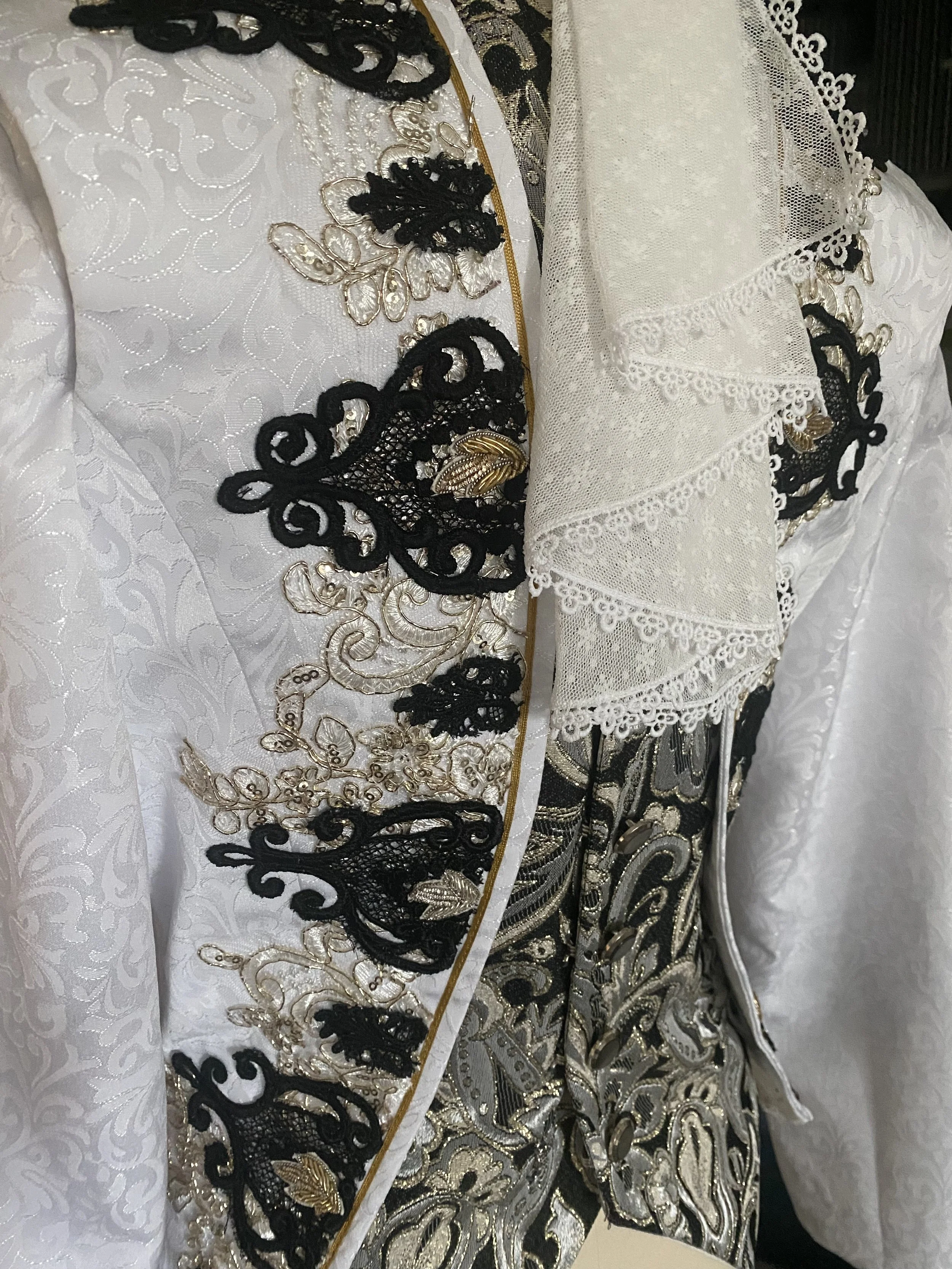 Close-up of ornate male ballet tunic with intricate gold and black embroidery, lace details, and layered fabric patterns.