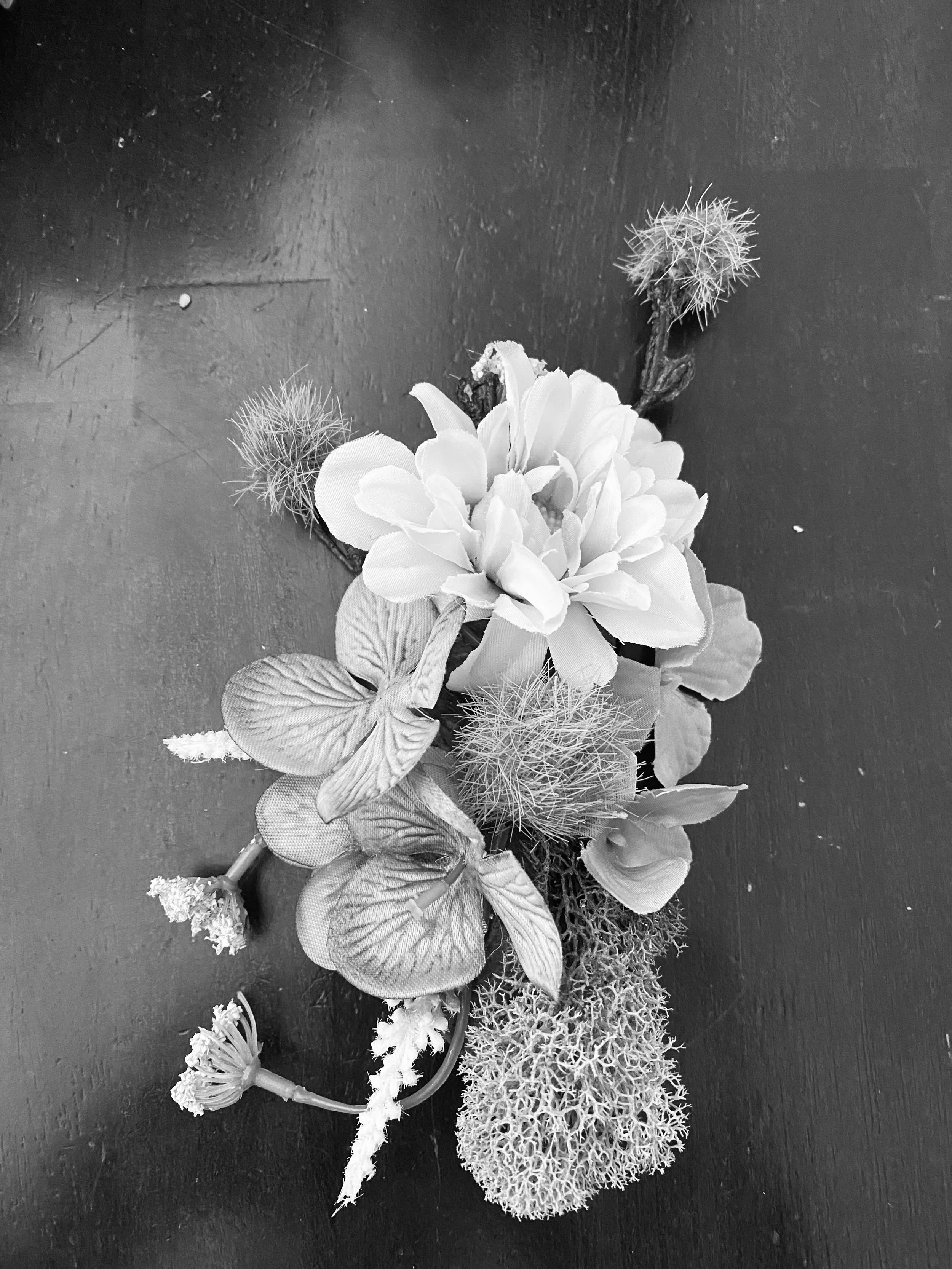 Black and white photo of a small floral arrangement with various flowers and dried plants on a dark surface.