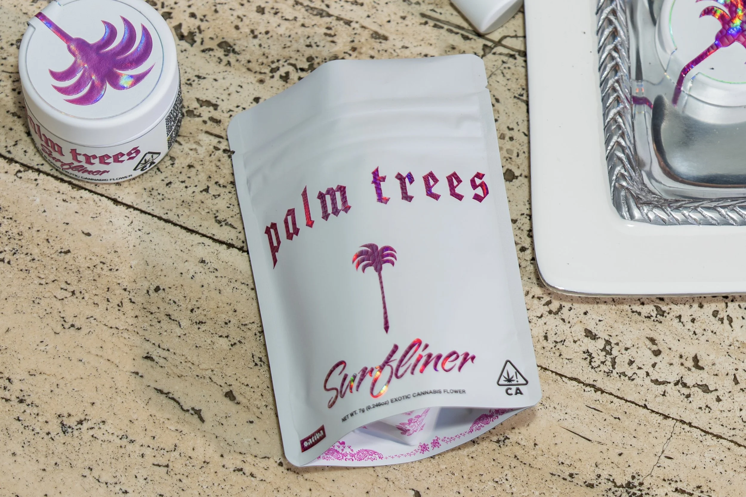 A white package with pink and purple text reading 'dallo tres' and a purple palm tree design, placed on a beige granite countertop with a silver tray and electrical outlet nearby.