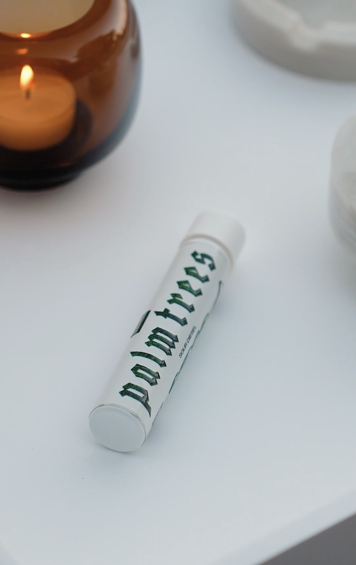 A white marker with green Gothic-style lettering sitting on a white surface, with a brown ceramic vase containing a lit candle and a white container in the background.