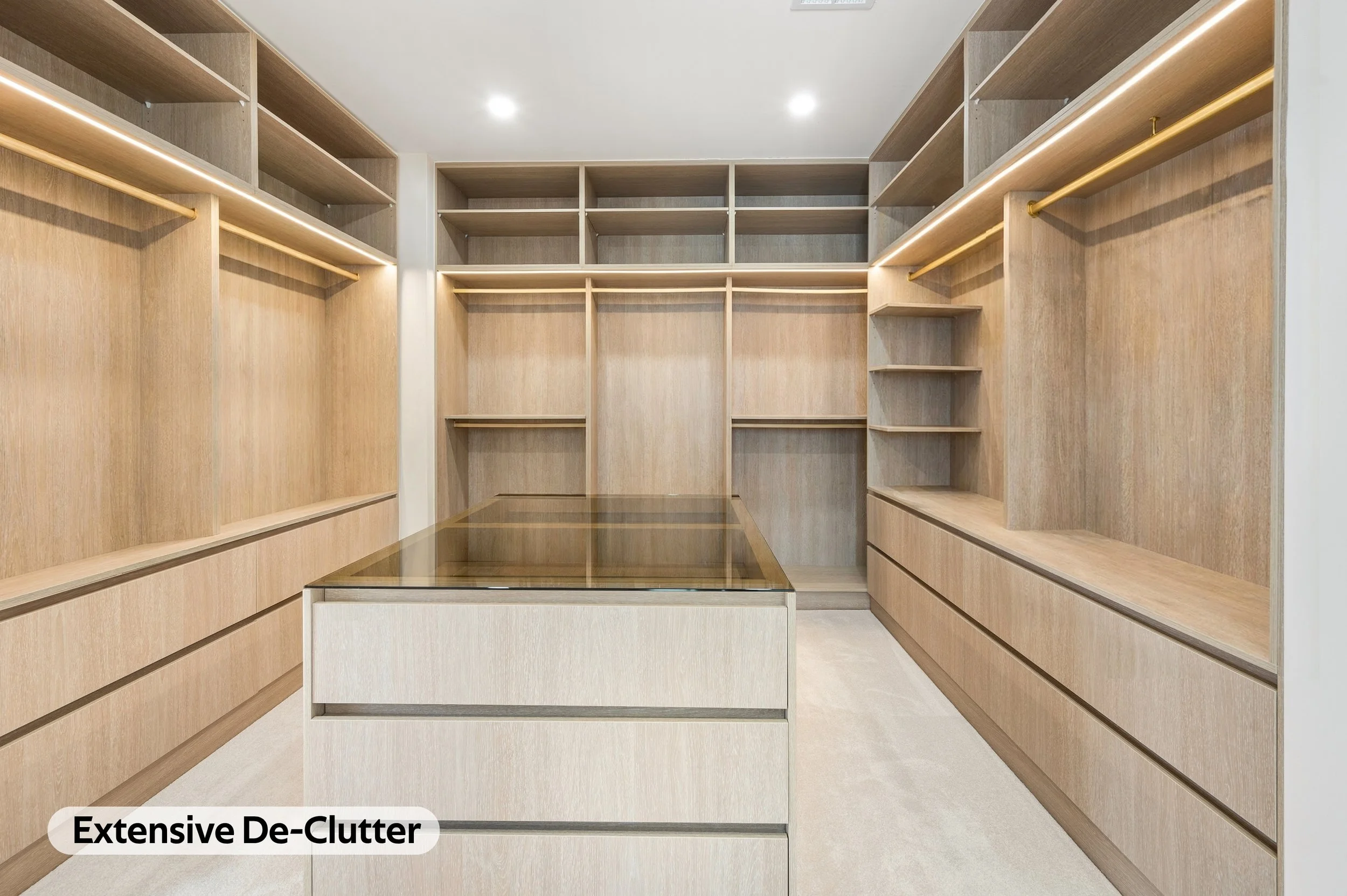 A spacious walk-in closet with extensive built-in wooden shelves and drawers for storage, featuring a central island with a glass top and ample lighting.