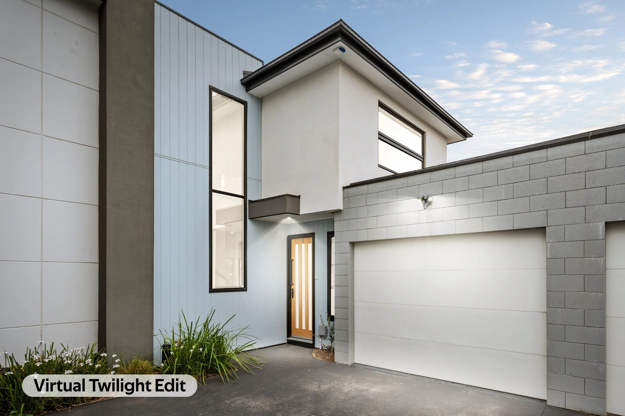 Modern house with white and gray exterior walls, large windows, and a wooden front door, under a partly cloudy sky.