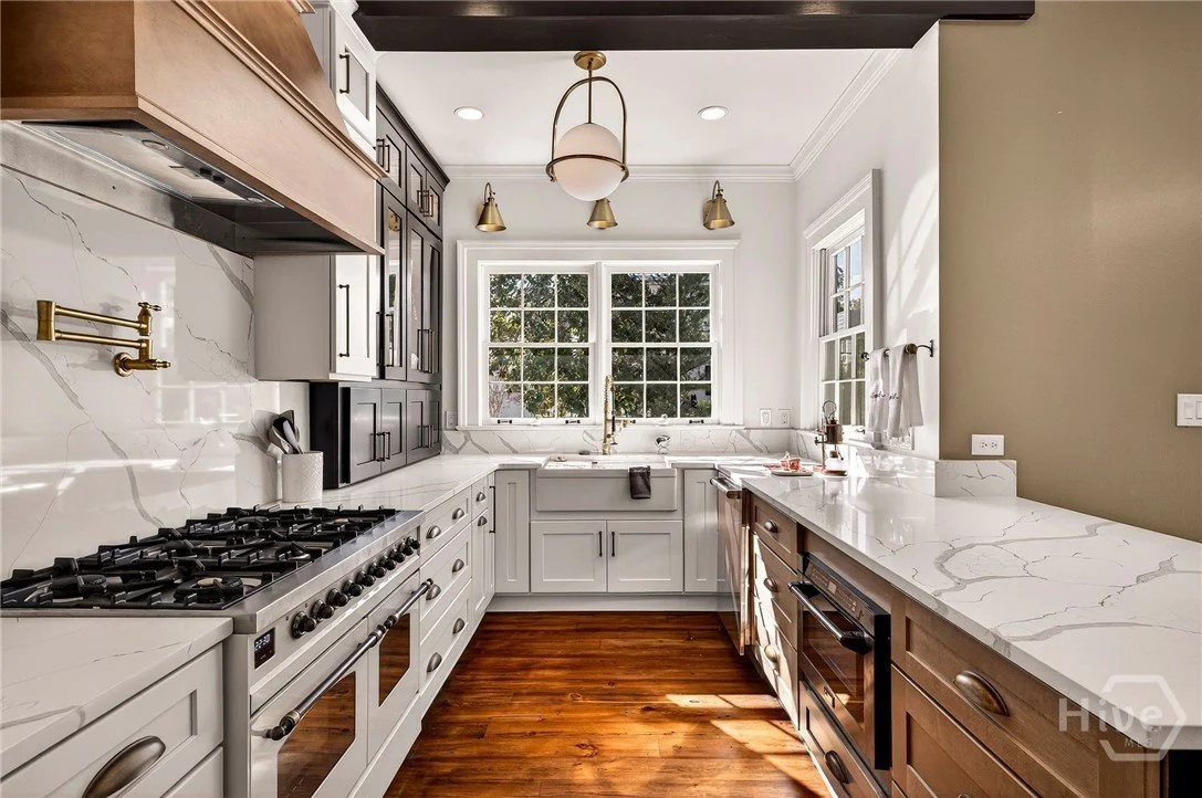 Bright kitchen with white and wood cabinetry, marble countertops, a window above the sink, and hardwood floors.
