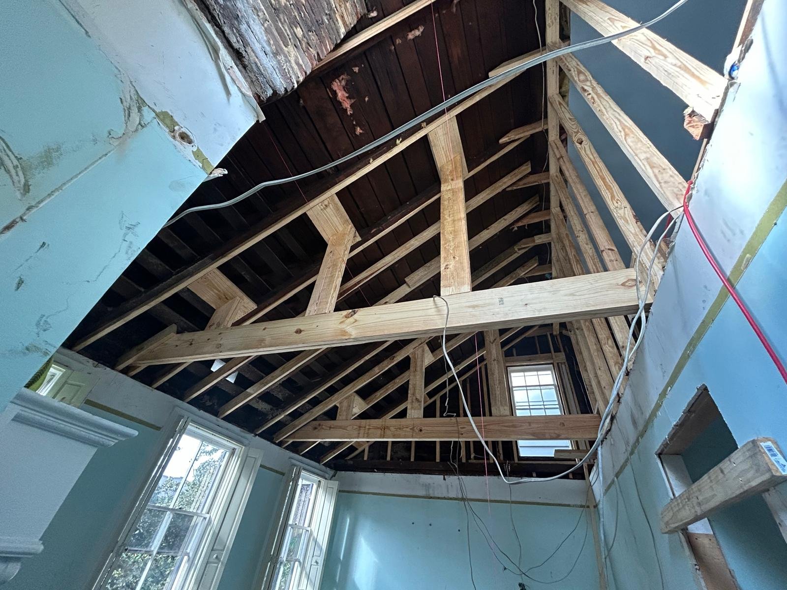 Interior of a house under construction with exposed wooden roof trusses and insulation. Windows are visible at the bottom of the image.