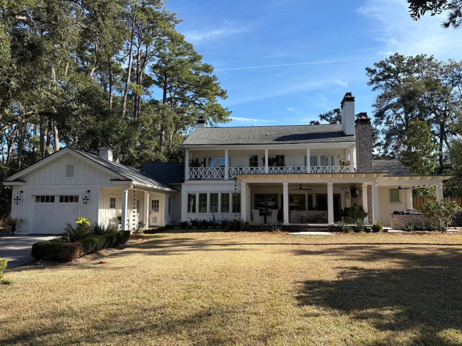 A large two-story white house with a front porch, surrounded by a grassy yard, trees in the background, and a clear blue sky.