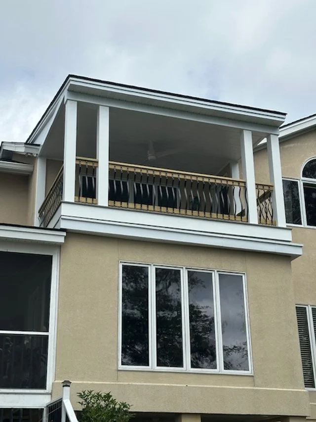 Exterior view of a three-story house featuring a lower level with large windows and an upper deck with white pillars and a protective railing.