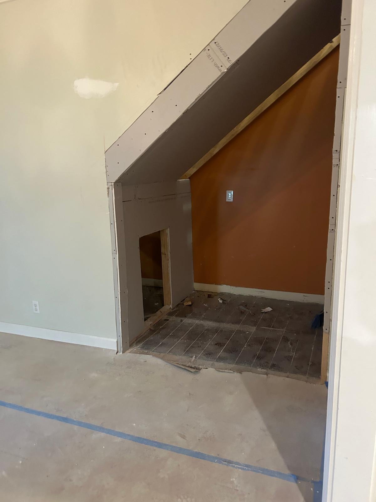 Construction site showing an unfinished interior wall with drywall, a small doorway, and a bathroom opening, with a brown wall and tiled floor.