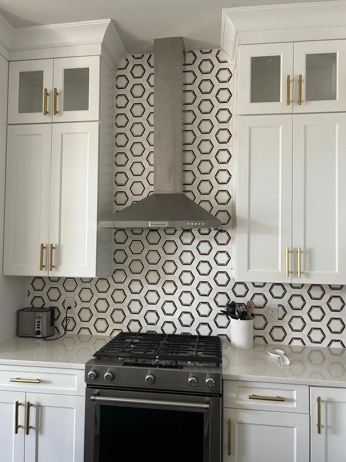 Kitchen with white cabinets, a stainless steel stove, a patterned tile backsplash, a stainless steel range hood, a small appliance on the left counter, and a utensil holder on the right counter.