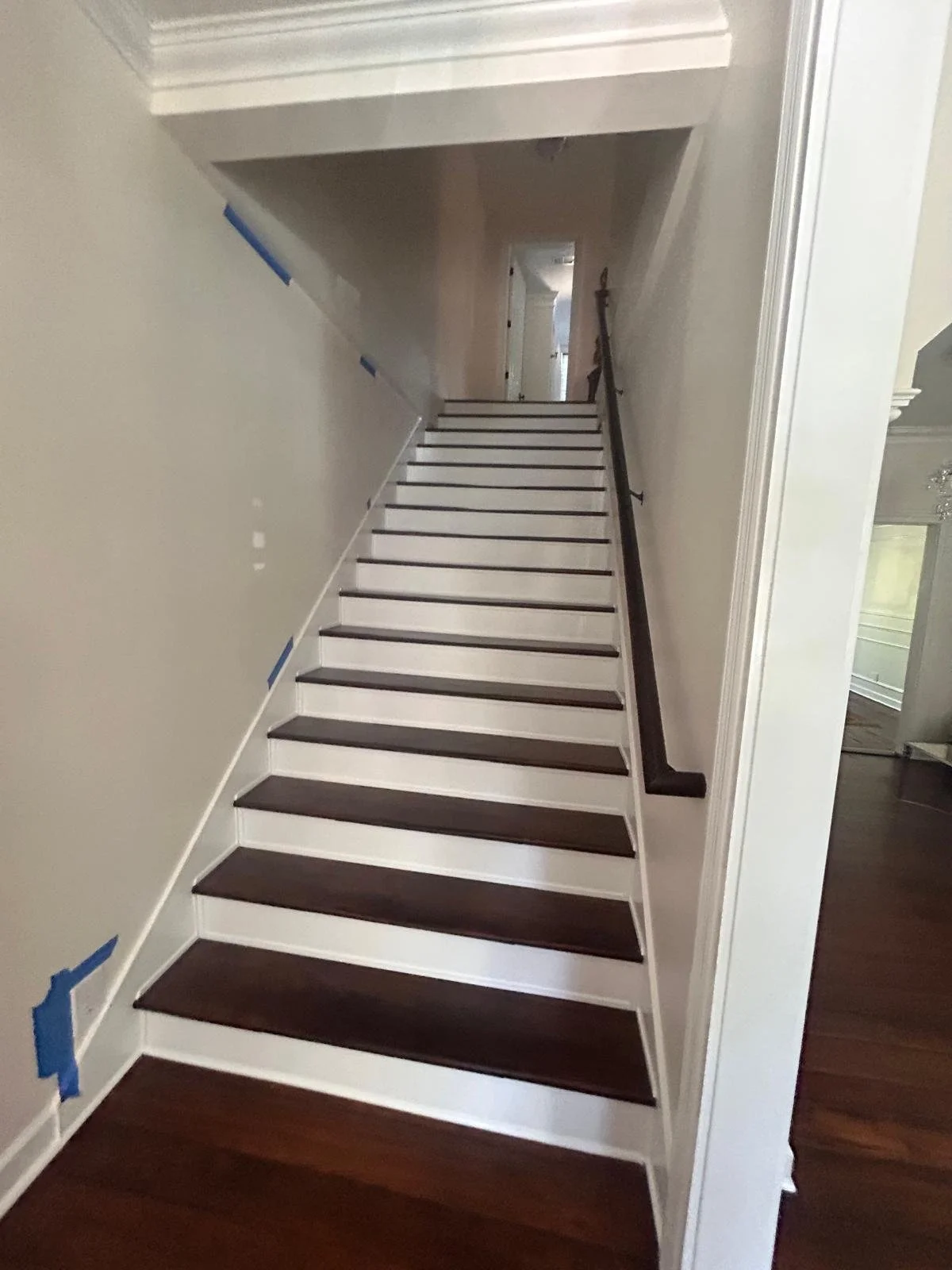 Interior view of a staircase with dark wood steps, black handrail on the right, and beige walls, leading to a hallway.