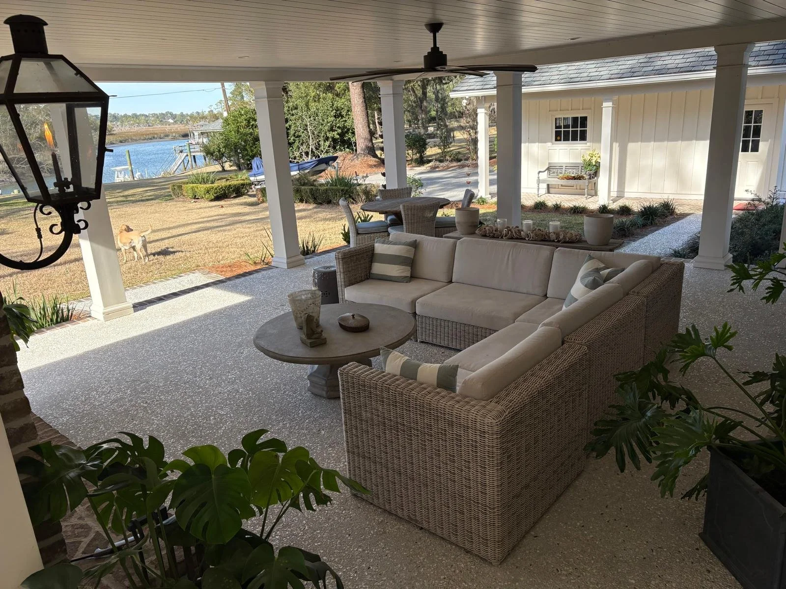 Outdoor covered patio with wicker sectional sofa and striped cushions, round coffee table, view of yard, water, boat, and dog