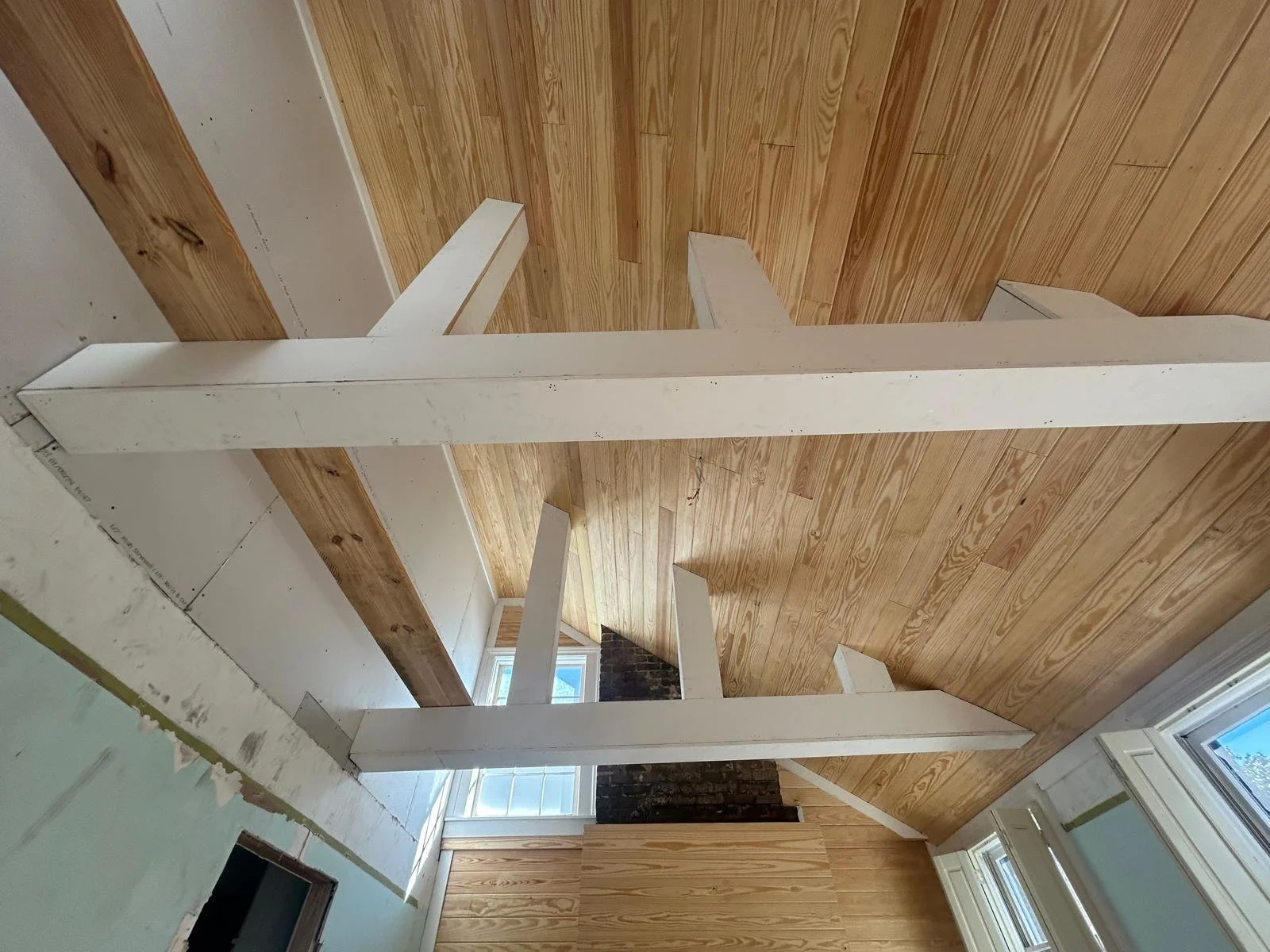 Interior of a house under renovation with white wooden beams, wooden wall paneling, and large windows.